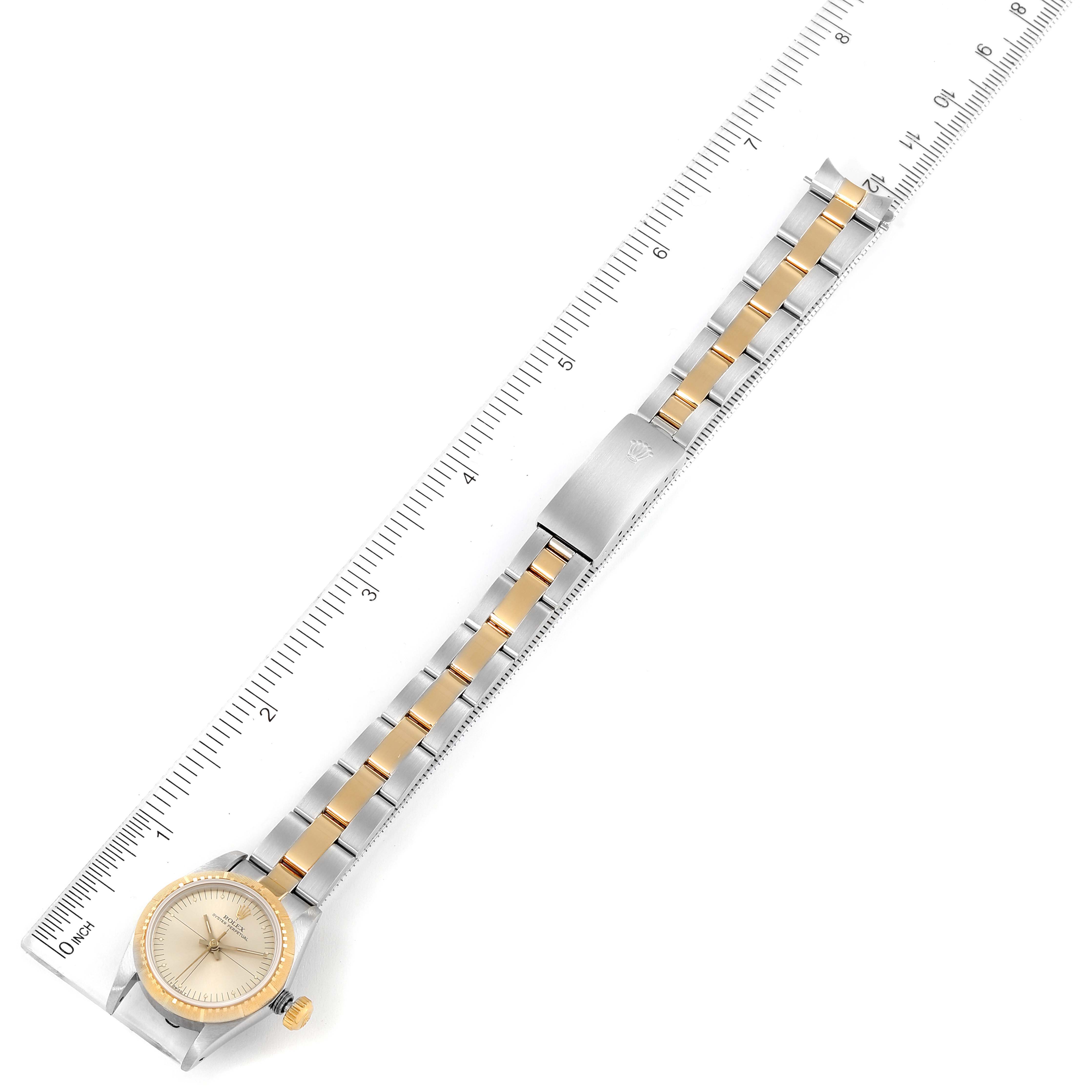 The image shows a top-down view of a Rolex Oyster Perpetual 67243 Women's Steel and Gold (two tone) Silver Dial 67243 Women's Steel and Gold (two tone) Silver Dial watch, including the face, band, and clasp, positioned next to a ruler.
