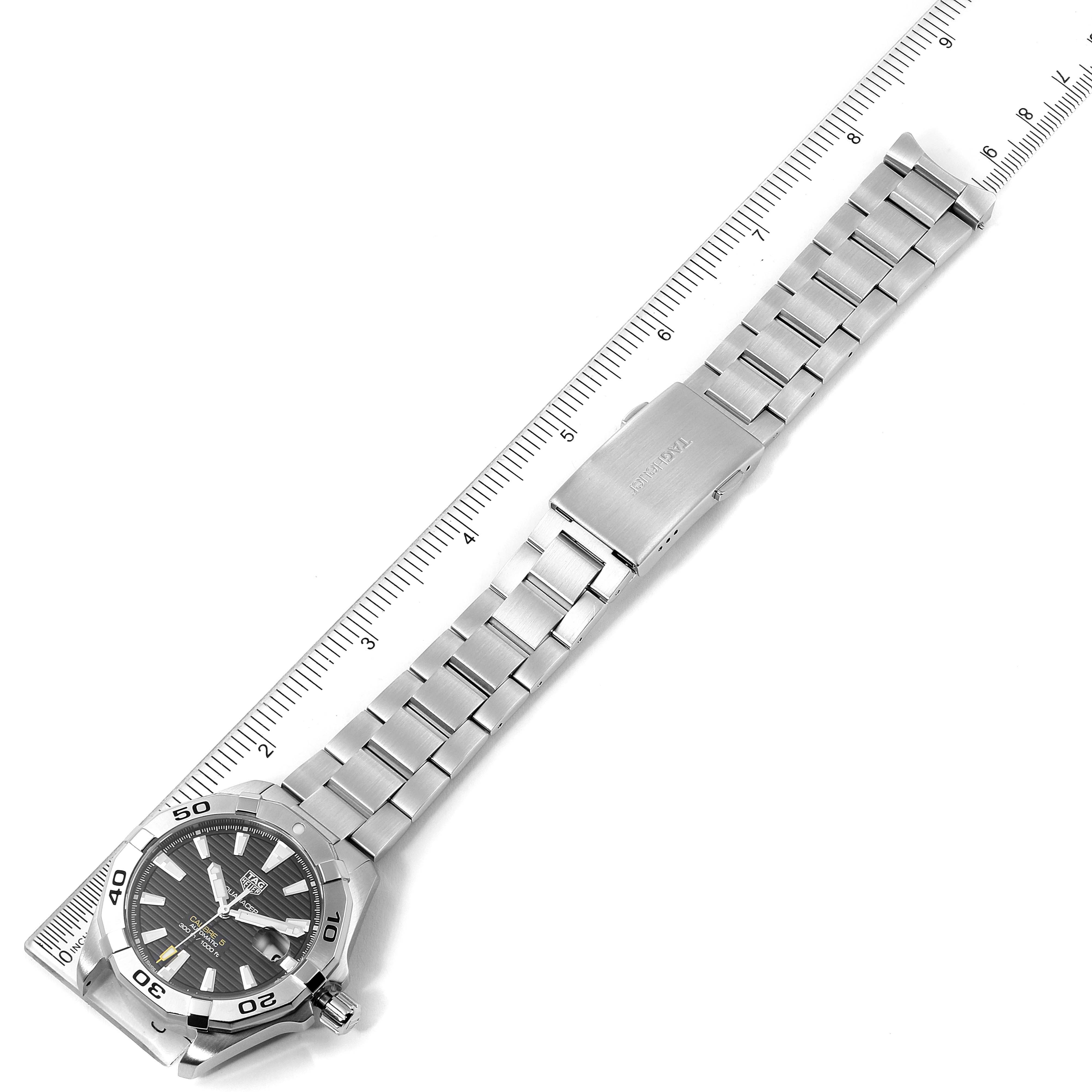 The image shows the Tag Heuer Aquaracer WBD2110.BA0928 Men
s Stainless Steel Black Dial WBD2110.BA0928 Men
s Stainless Steel Black Dial watch laid flat, highlighting its metal band, clasp, and watch face next to a ruler.