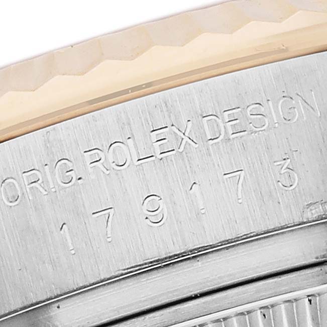 The image shows a close-up of a Rolex Datejust 179173 Women's Steel and Gold (two tone) Silver Dial 179173 Women's Steel and Gold (two tone) Silver Dial model's side case with engraved text and a partial view of the bezel.