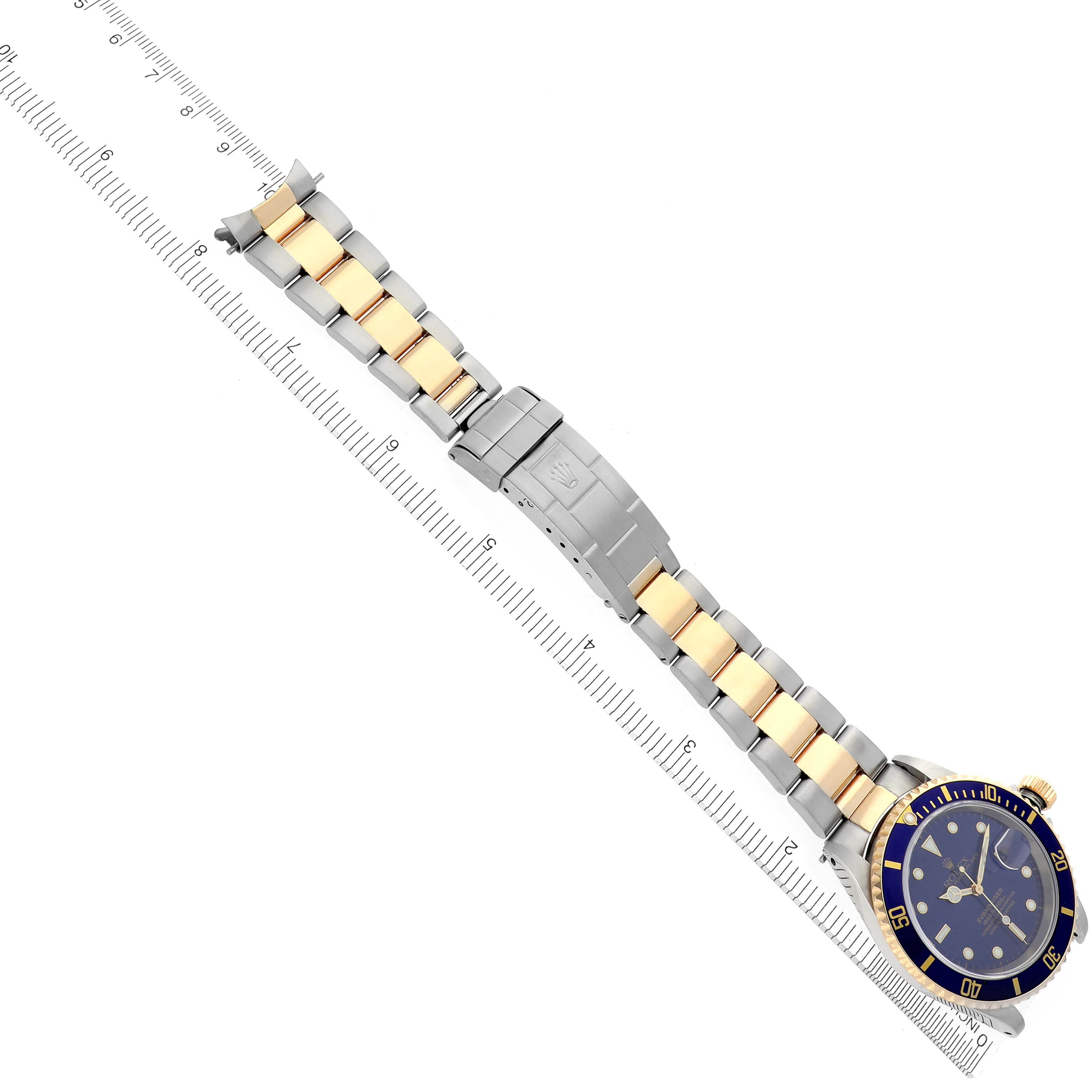 The image shows a top-down view of a Rolex Submariner 16613 Men's Steel and Gold (two tone) Blue Dial 16613 Men's Steel and Gold (two tone) Blue Dial with its bracelet and clasp fully extended, aligned alongside a ruler.
