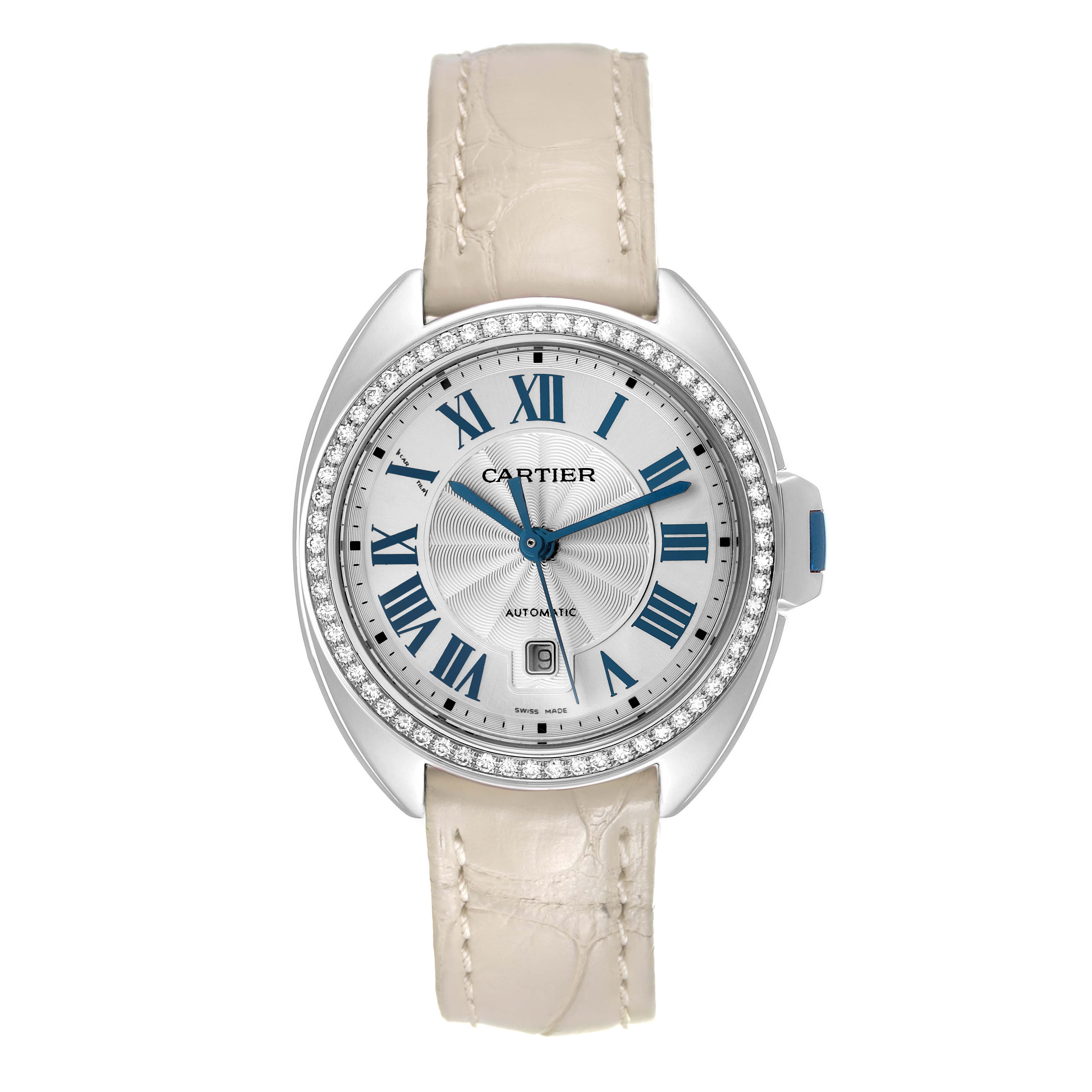 The Cartier Clé watch is shown head-on, featuring a diamond bezel, silver dial with blue Roman numerals, and a beige leather strap.