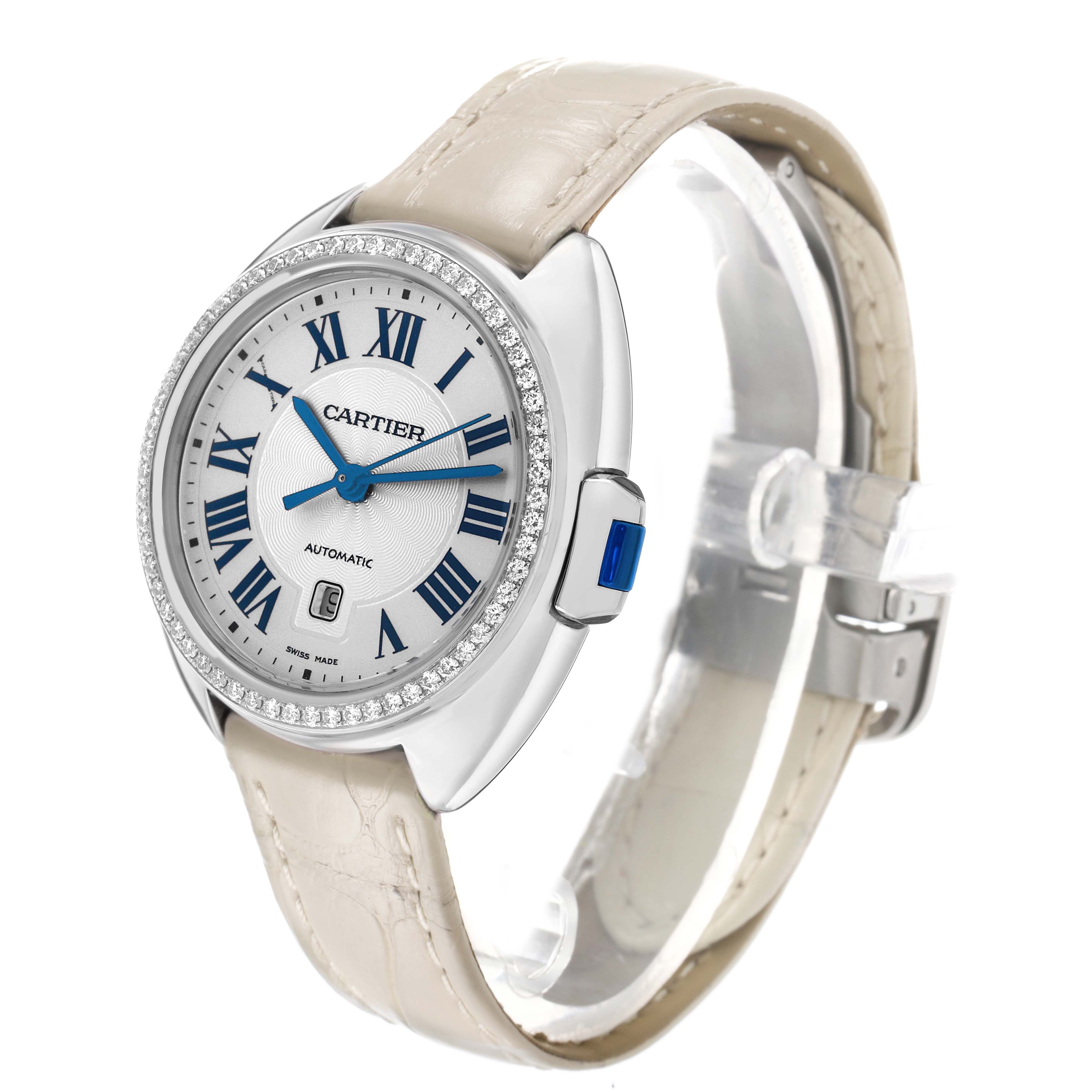 The Cartier Clé watch is shown at a slight angle, highlighting the dial, diamond-set bezel, and leather strap.