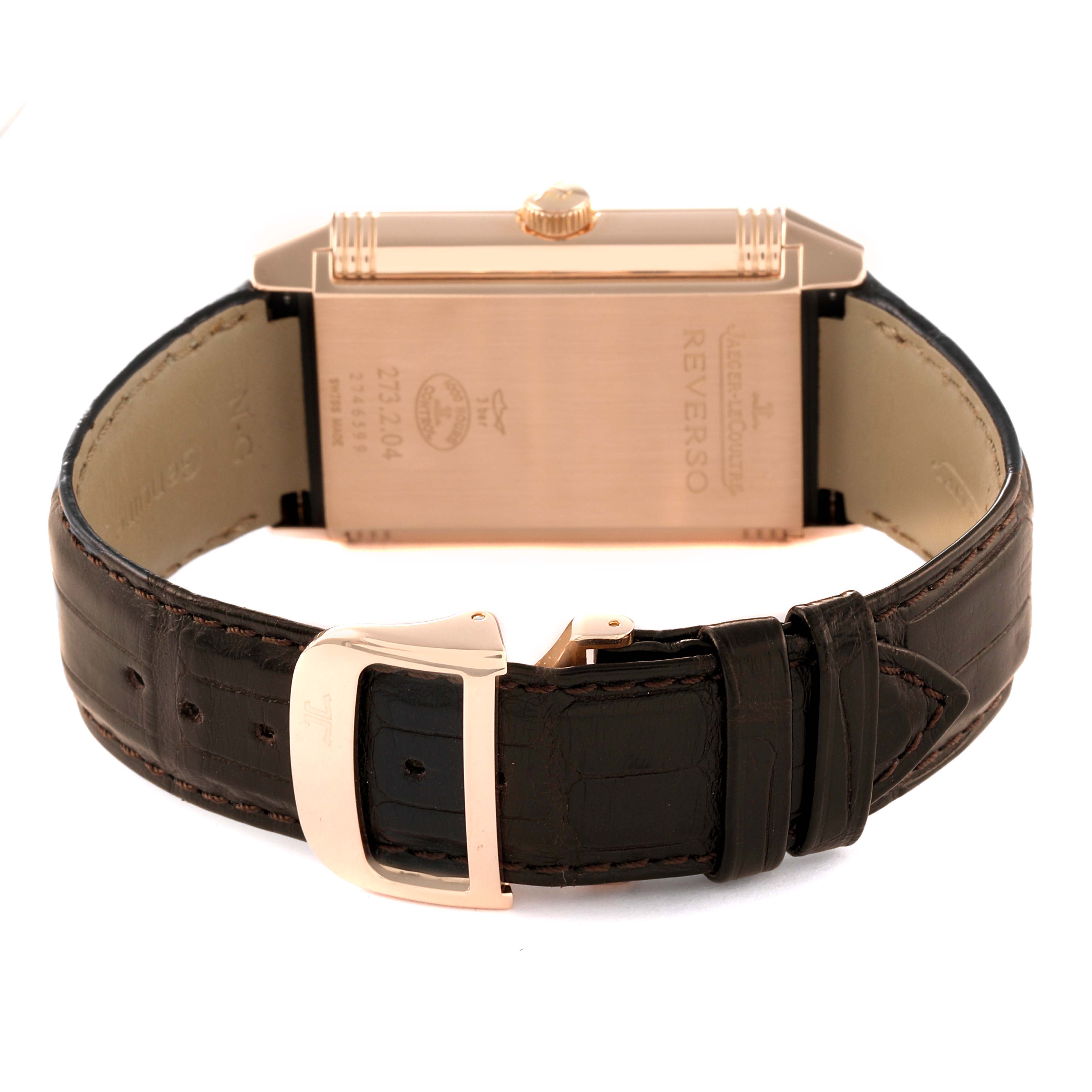 This image shows the back of a Jaeger-LeCoultre Reverso watch and its brown leather strap with a gold buckle.