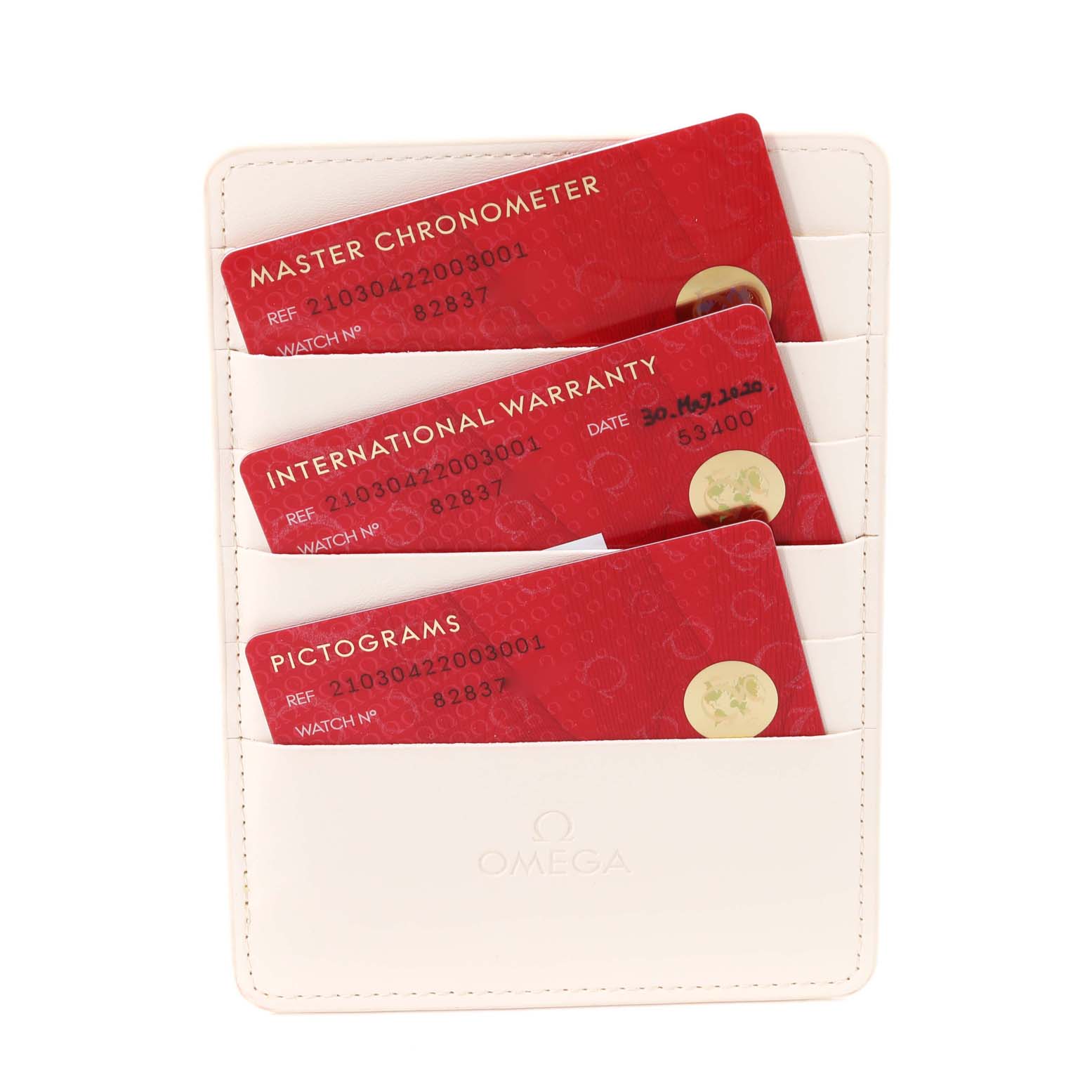 The image shows three red cards titled "Master Chronometer," "International Warranty," and "Pictograms" in a white Omega cardholder.