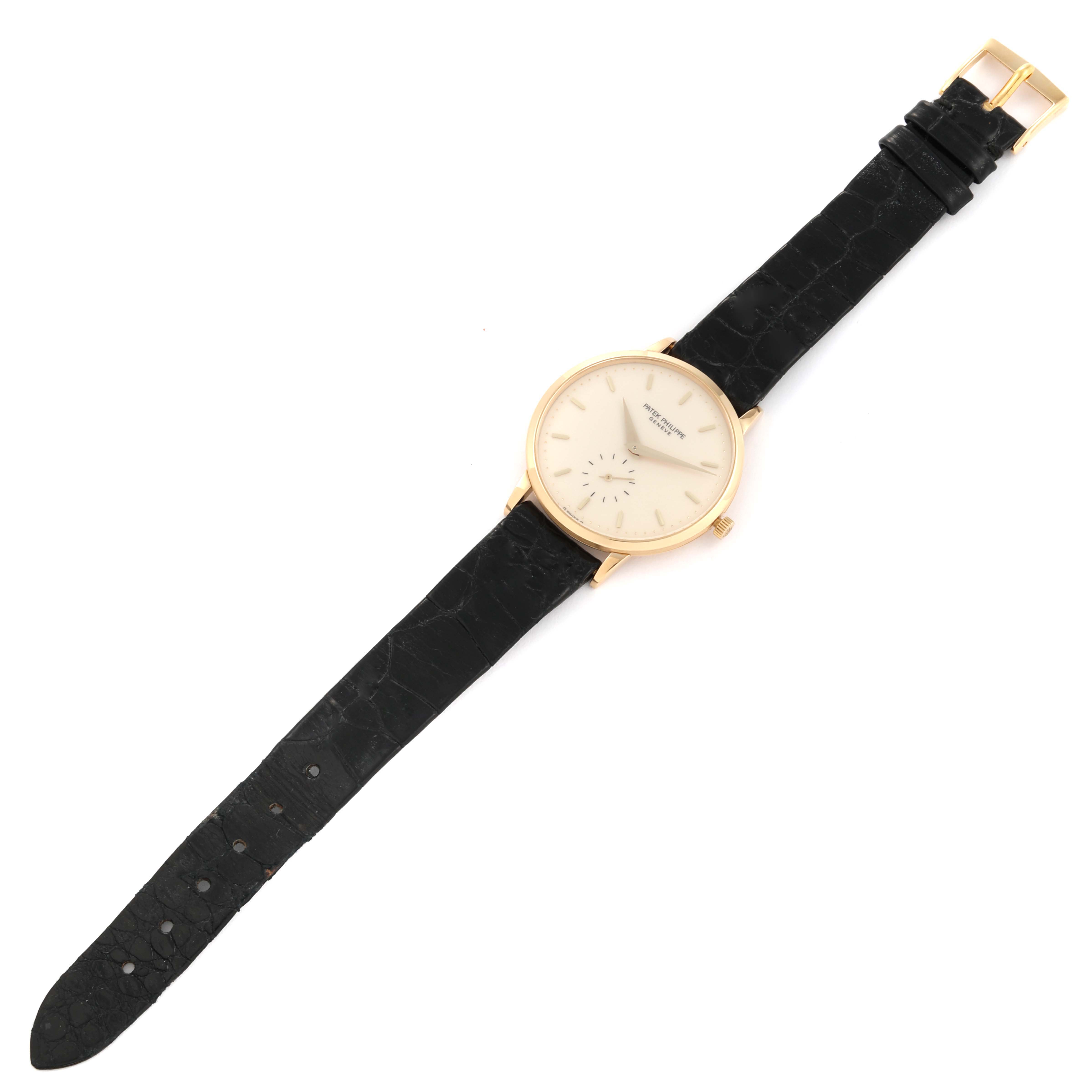 The Patek Philippe Calatrava 3893J Men
s Yellow Gold White Dial 3893J Men
s Yellow Gold White Dial watch is shown from a top-down angle, displaying the face, black leather strap, and gold buckle.