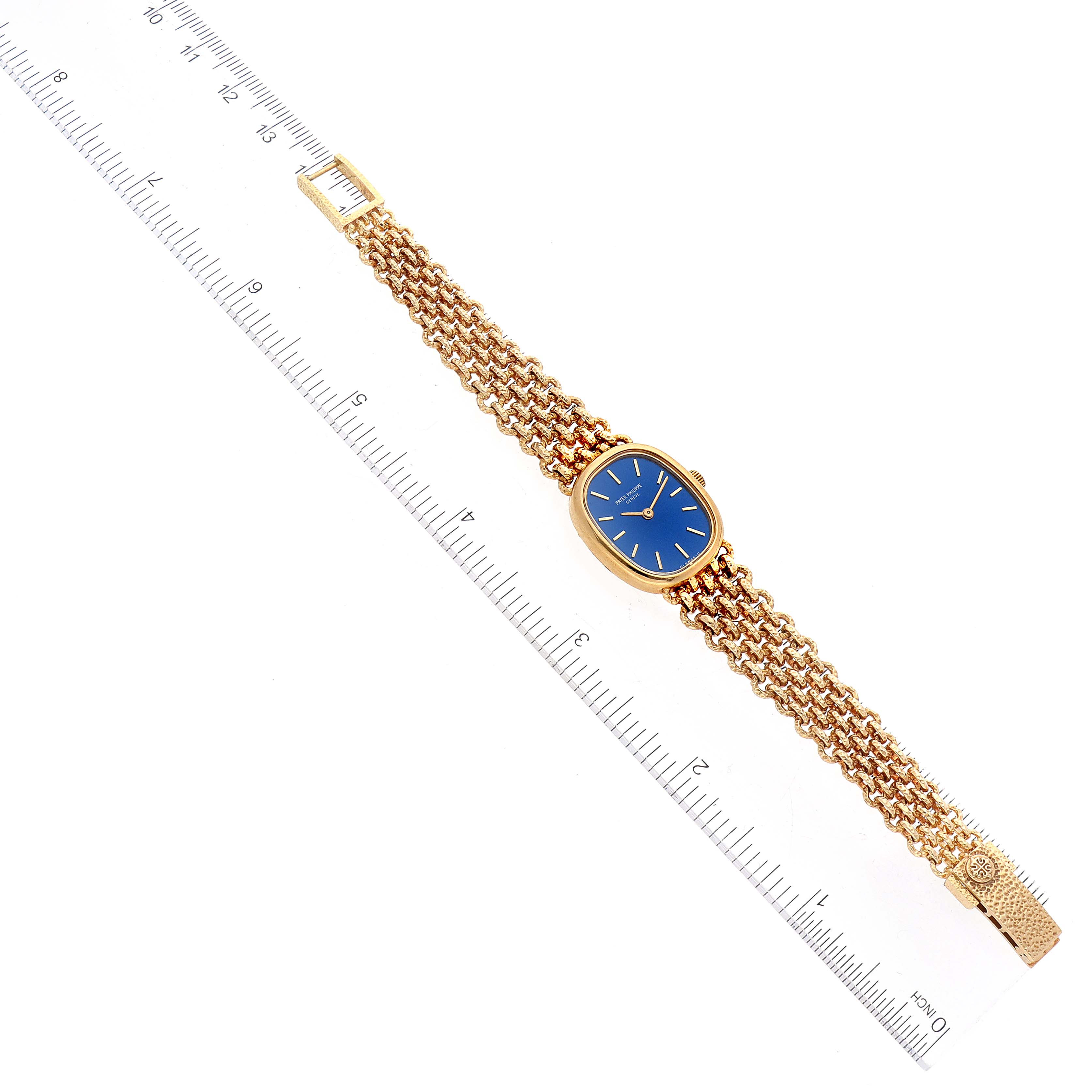 The image shows a full view of the Patek Philippe Golden Ellipse 4464/4 Women's Yellow Gold Blue Dial 4464/4 Women's Yellow Gold Blue Dial watch, including the face and gold bracelet, with a ruler for scale.
