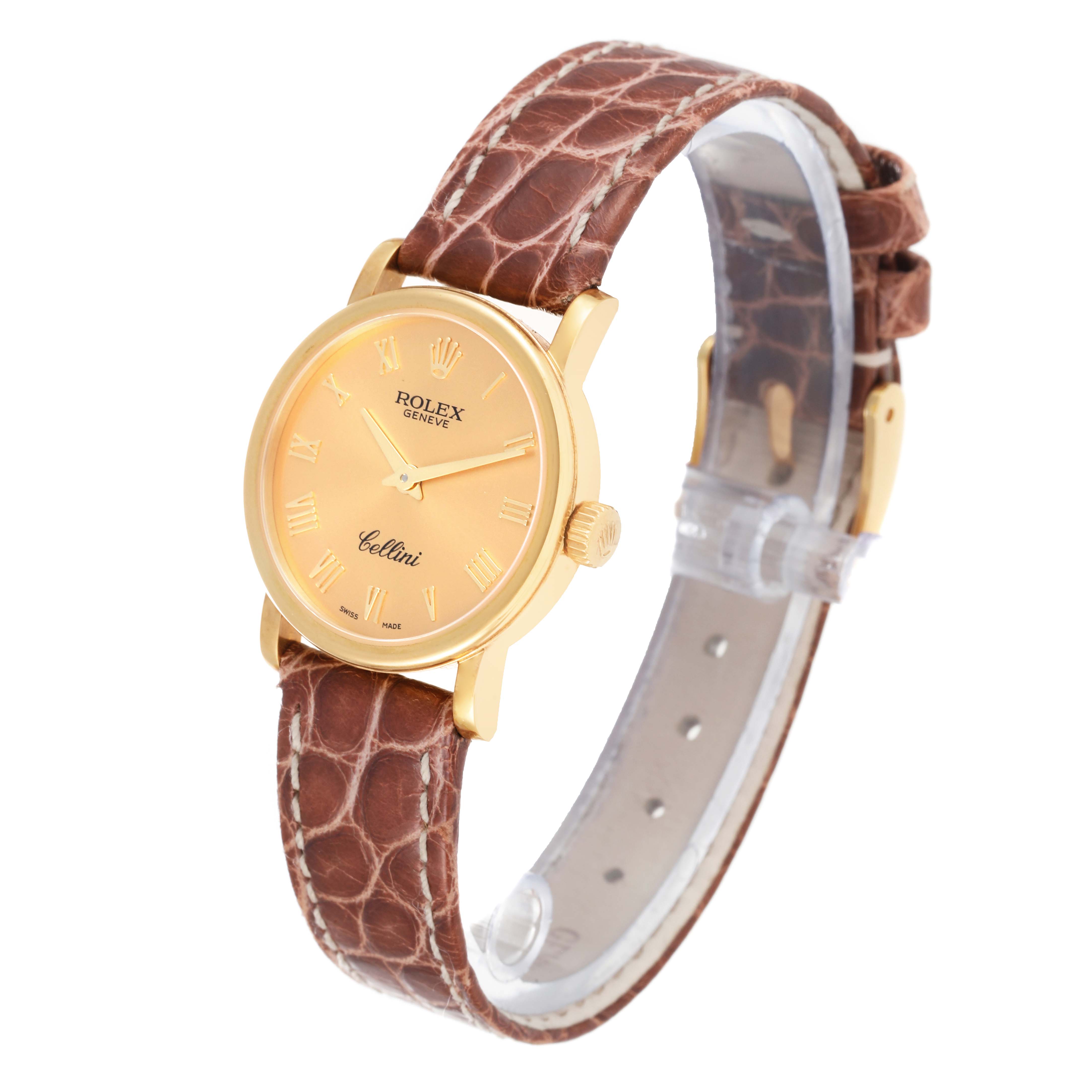 The Rolex Cellini 6110/8 Women's Yellow Gold Champagne Dial 6110/8 Women's Yellow Gold Champagne Dial watch is shown at a tilted front angle, displaying a round gold case, beige dial, and brown leather strap.