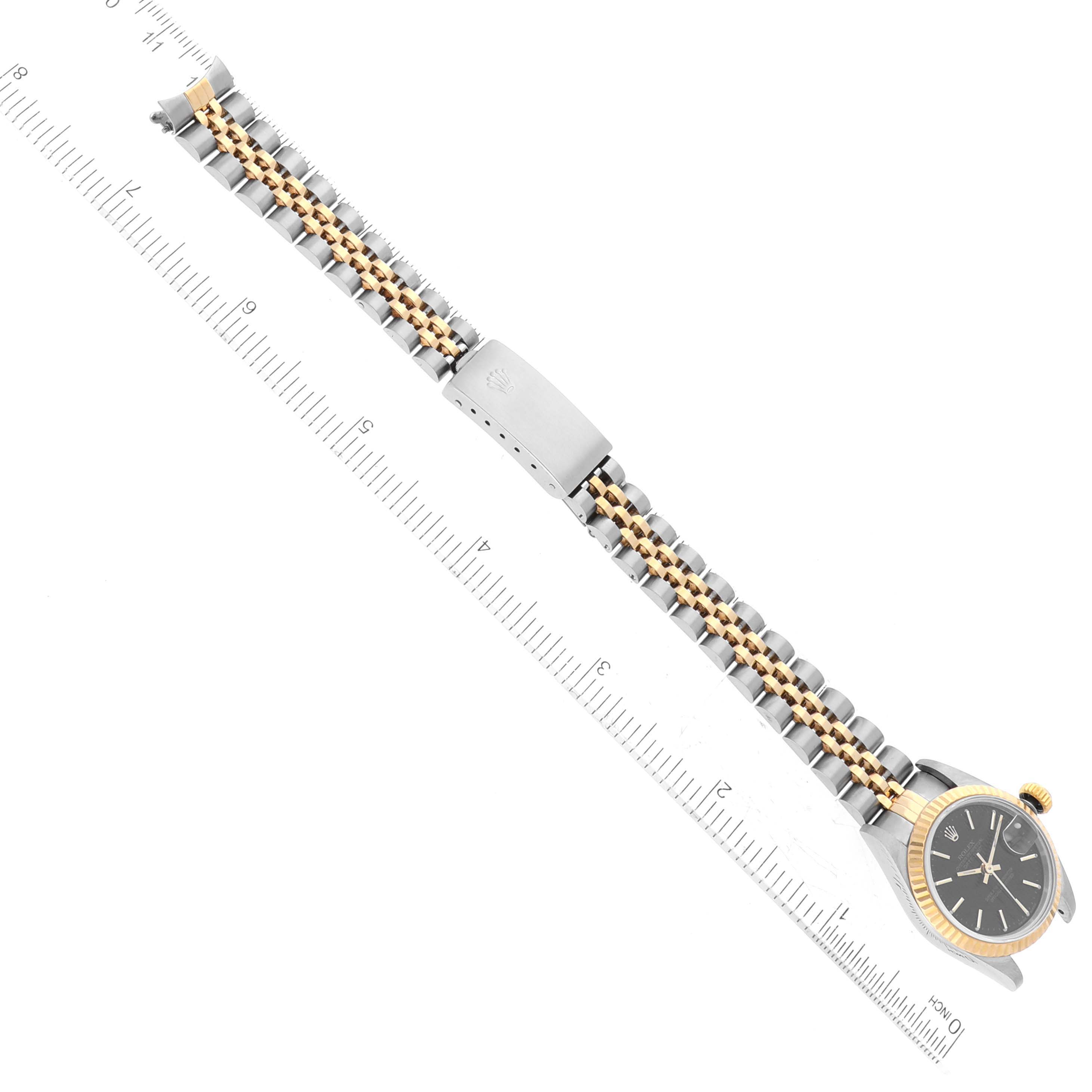The image shows a Rolex Datejust 69173 Women's Steel and Gold (two tone) Black Dial 69173 Women's Steel and Gold (two tone) Black Dial watch laid flat, with the face, bezel, and bracelet visible, alongside a ruler for scale.