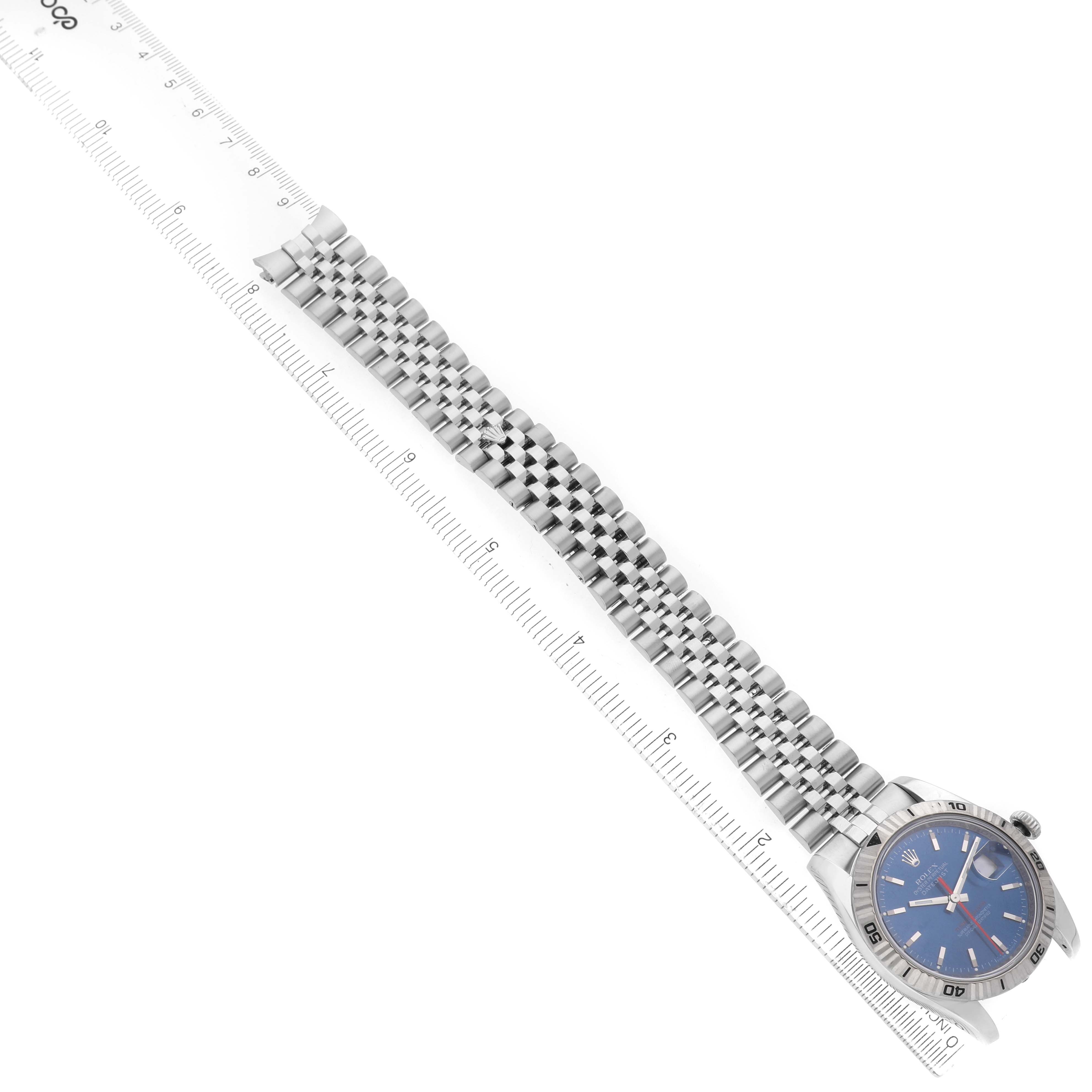 The image shows a Rolex Turn-o-Graph 116264 Men's Stainless Steel Blue Dial watch with a blue dial and silver bezel, placed diagonally with a bracelet and a ruler.