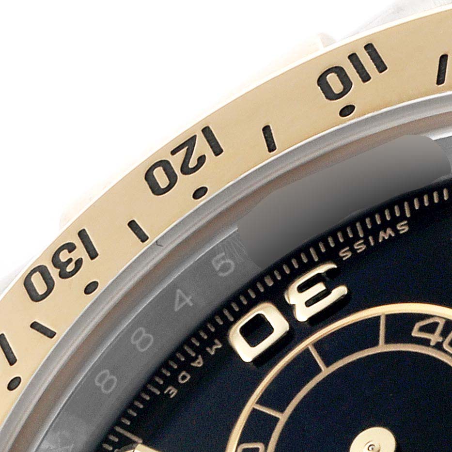 The image shows a close-up of the upper left section of the Rolex Daytona 116523 Men's Steel and Gold (two tone) Black Dial bezel and dial.