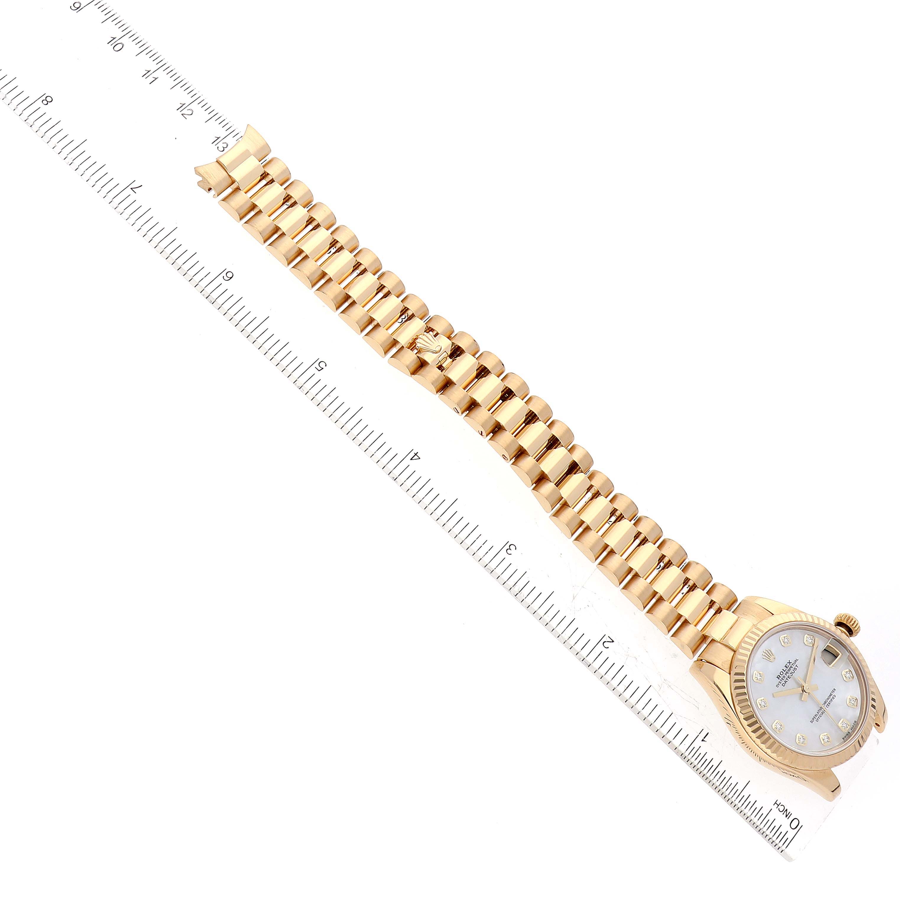The image shows a President model Rolex watch laying flat with its face and gold bracelet visible alongside a ruler.