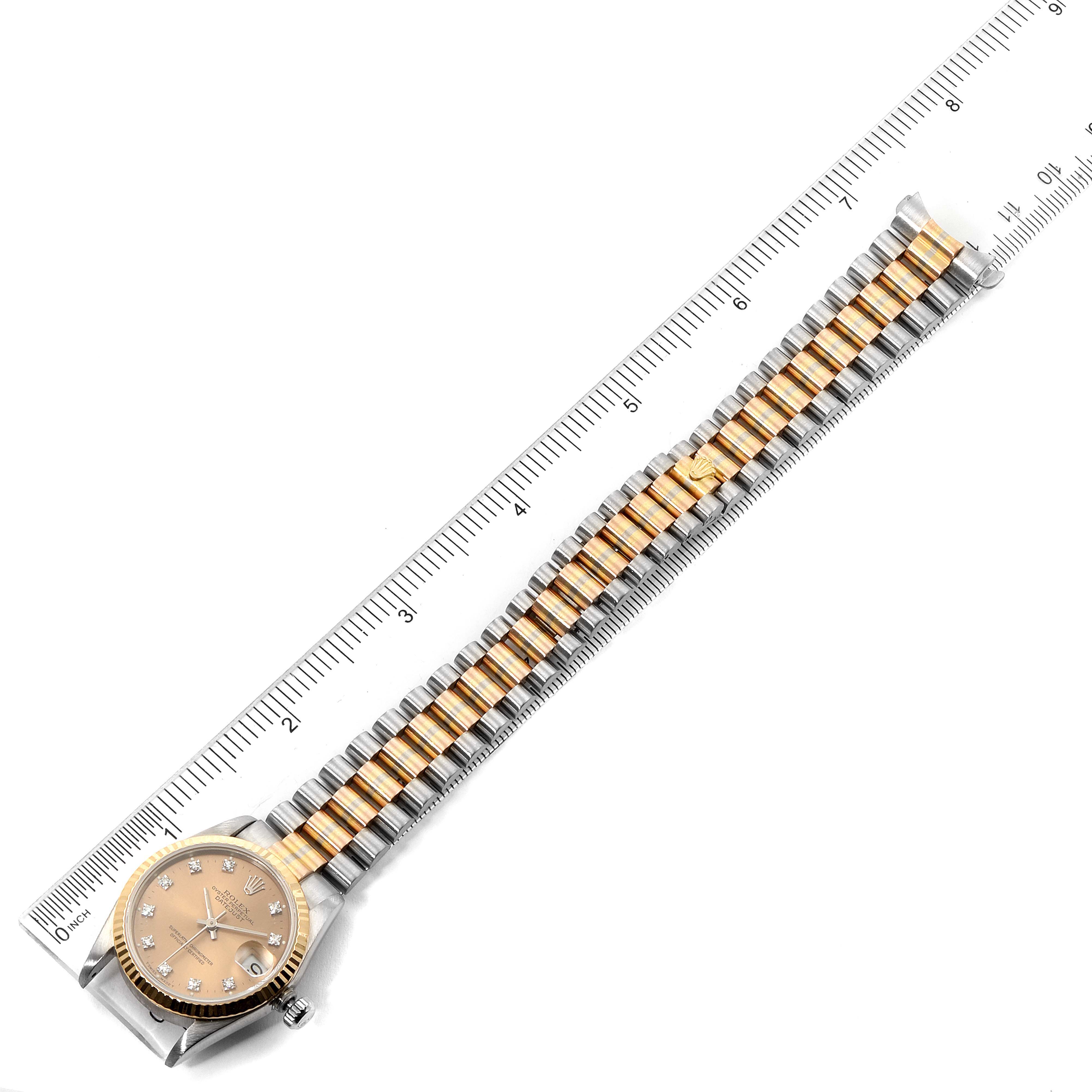 The Rolex President 68279 Women's White Gold Brown Dial 68279 Women's White Gold Brown Dial model watch is shown from a top-down angle, displaying the face and the entire bracelet lying alongside a ruler.