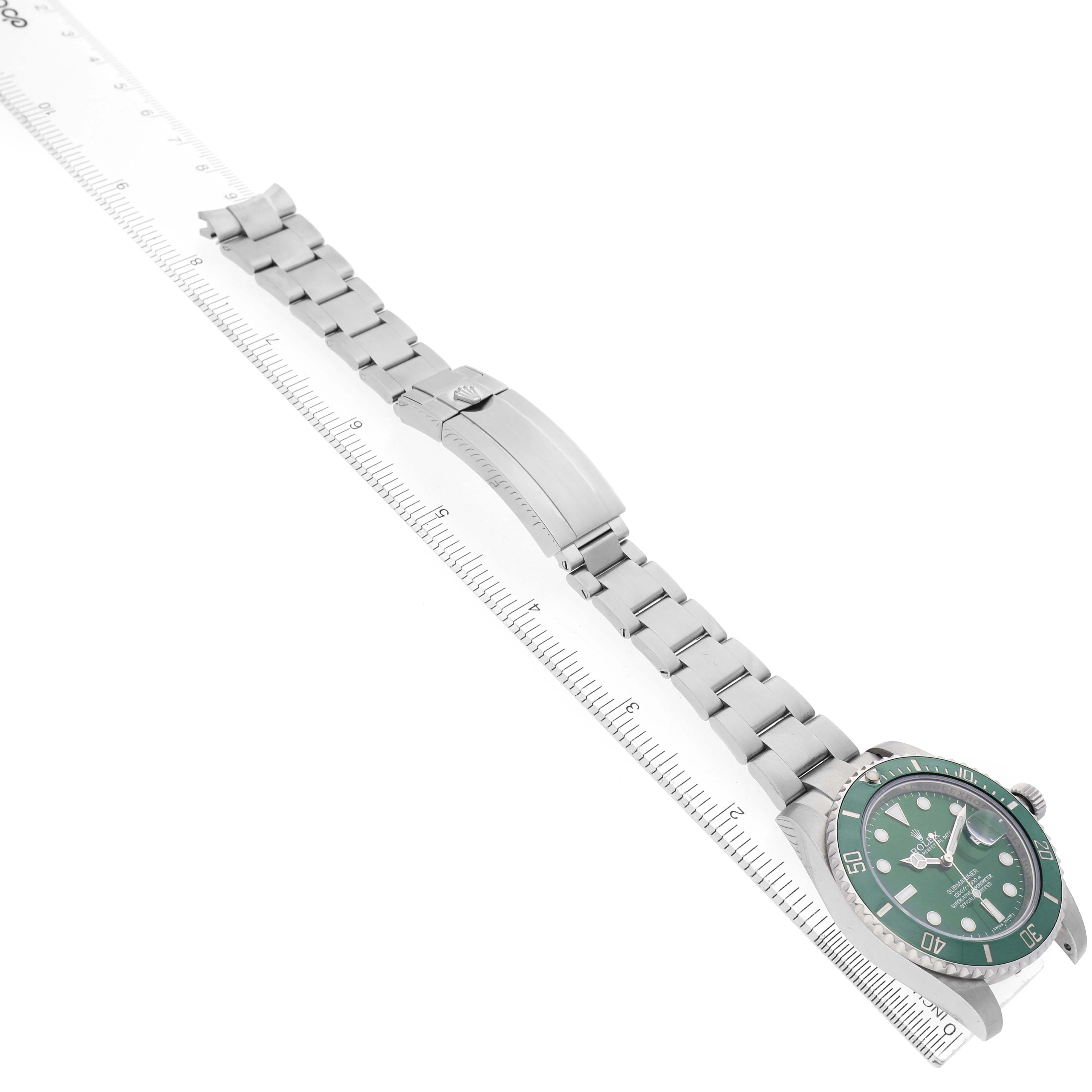 The Rolex Submariner 116610LV Men's Stainless Steel Green Dial watch is shown at an angle, displaying the dial, bracelet, and clasp alongside a measuring ruler.