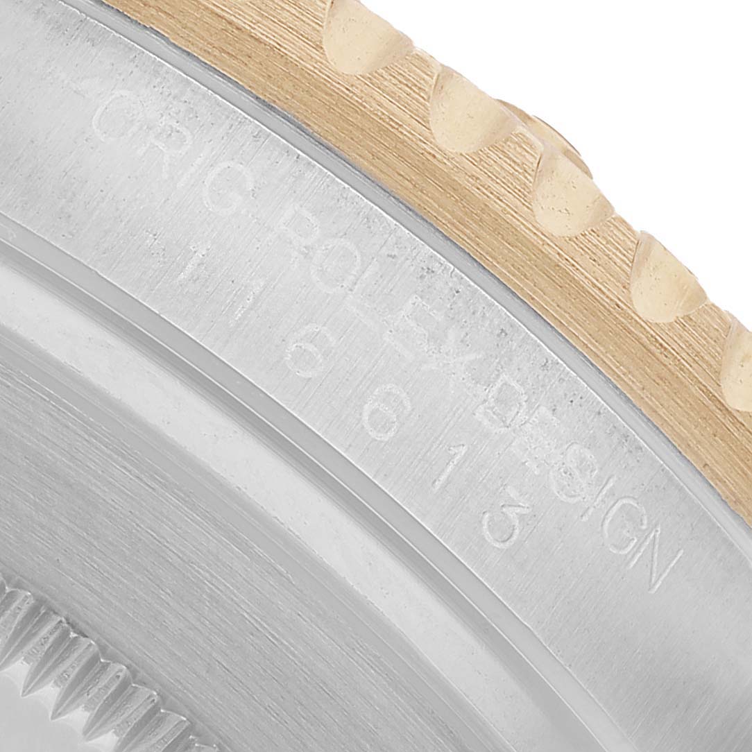 The image shows a close-up of the Rolex Submariner 116613 Men's Steel and Gold (two tone) Black Dial's bezel and engraved edge at an angle, highlighting its design details.