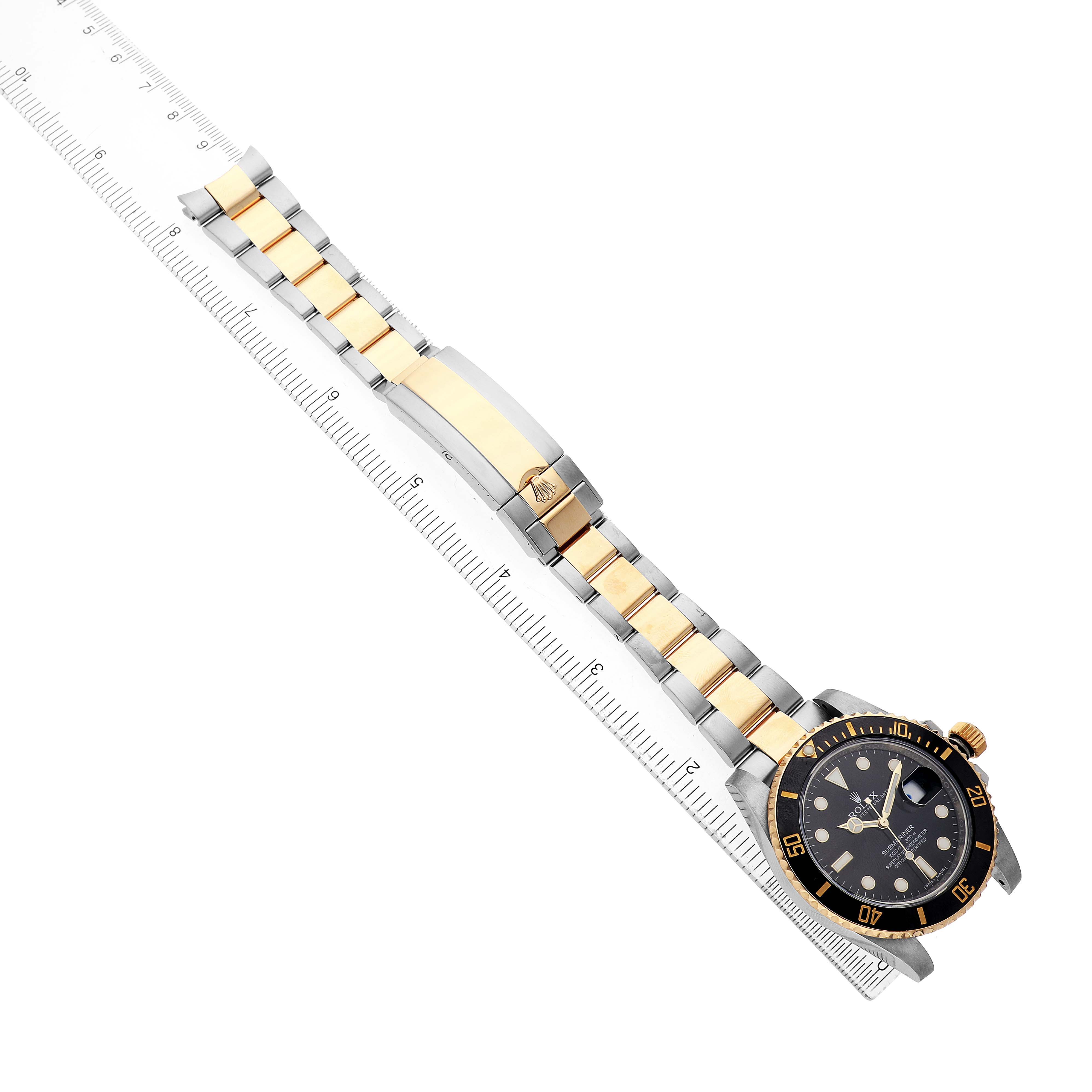 The Rolex Submariner 116613 Men's Steel and Gold (two tone) Black Dial is displayed diagonally, showing the full bracelet and face, alongside a ruler for scale.