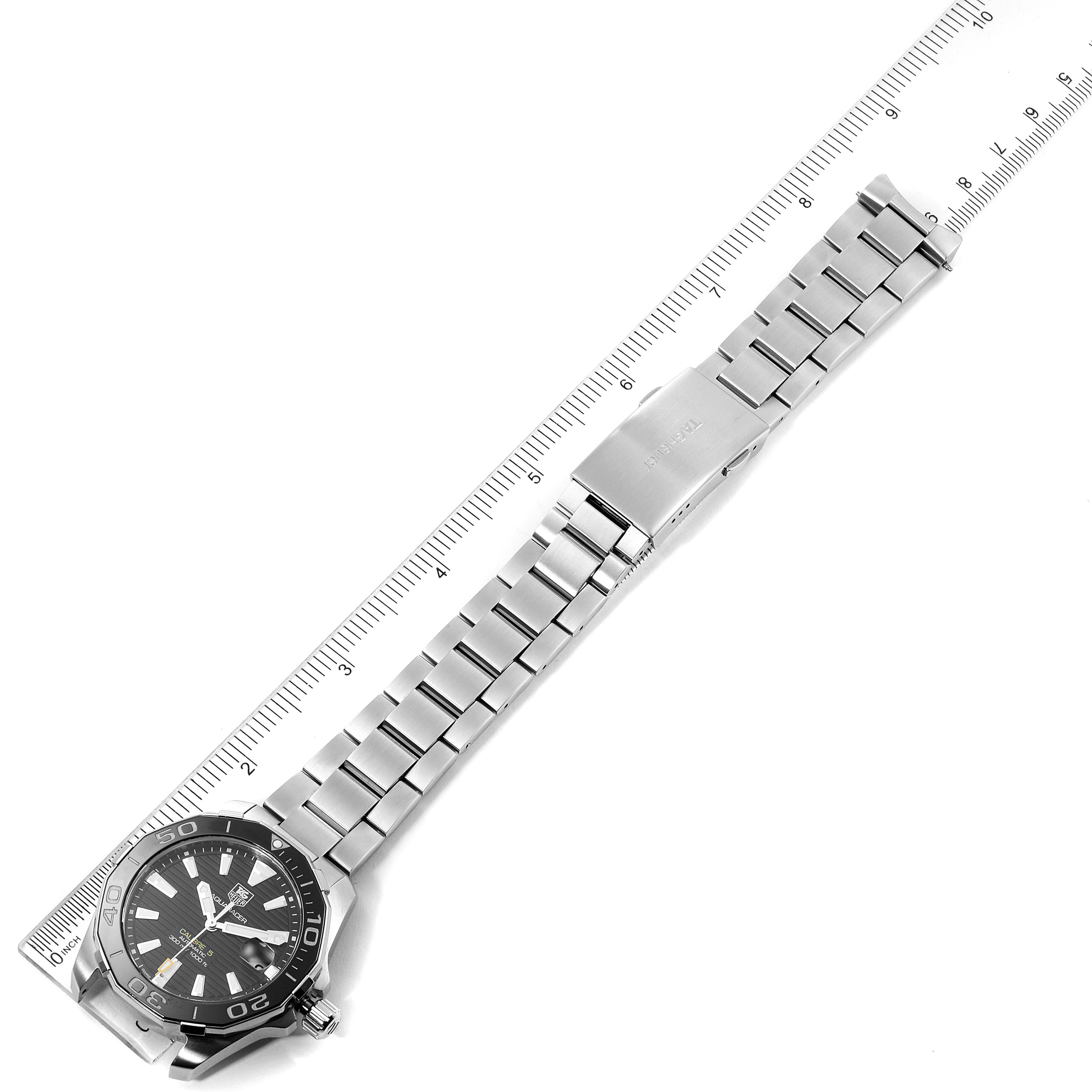 The image shows a Tag Heuer Aquaracer WAY211A Men's Stainless Steel Black Dial WAY211A Men's Stainless Steel Black Dial watch laid flat along a ruler, displaying its black dial, bezel, and metal bracelet.