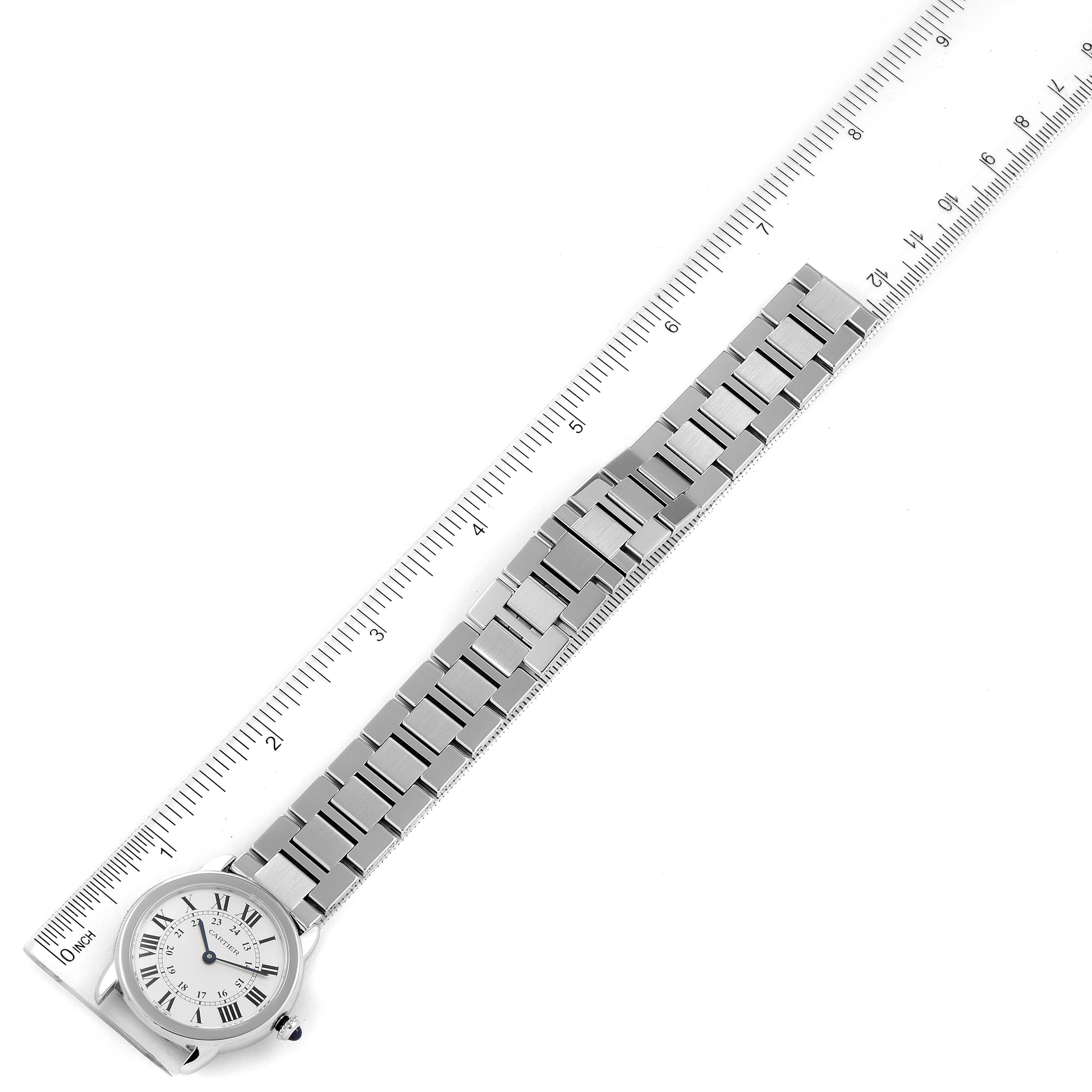 The image shows a top-down view of a Cartier Ronde W6701004 Women
s Stainless Steel Silver Dial W6701004 Women
s Stainless Steel Silver Dial watch with its metal bracelet positioned beside a ruler.