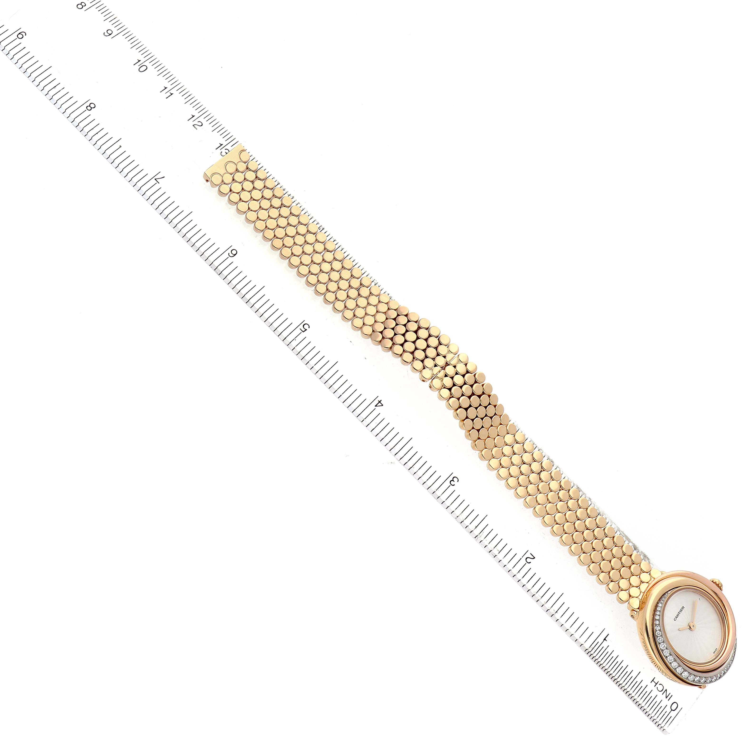 The Cartier Trinity WG200258 Women's Yellow Gold White Dial watch is shown from a top view, displaying its round face and textured bracelet alongside a ruler for scale.