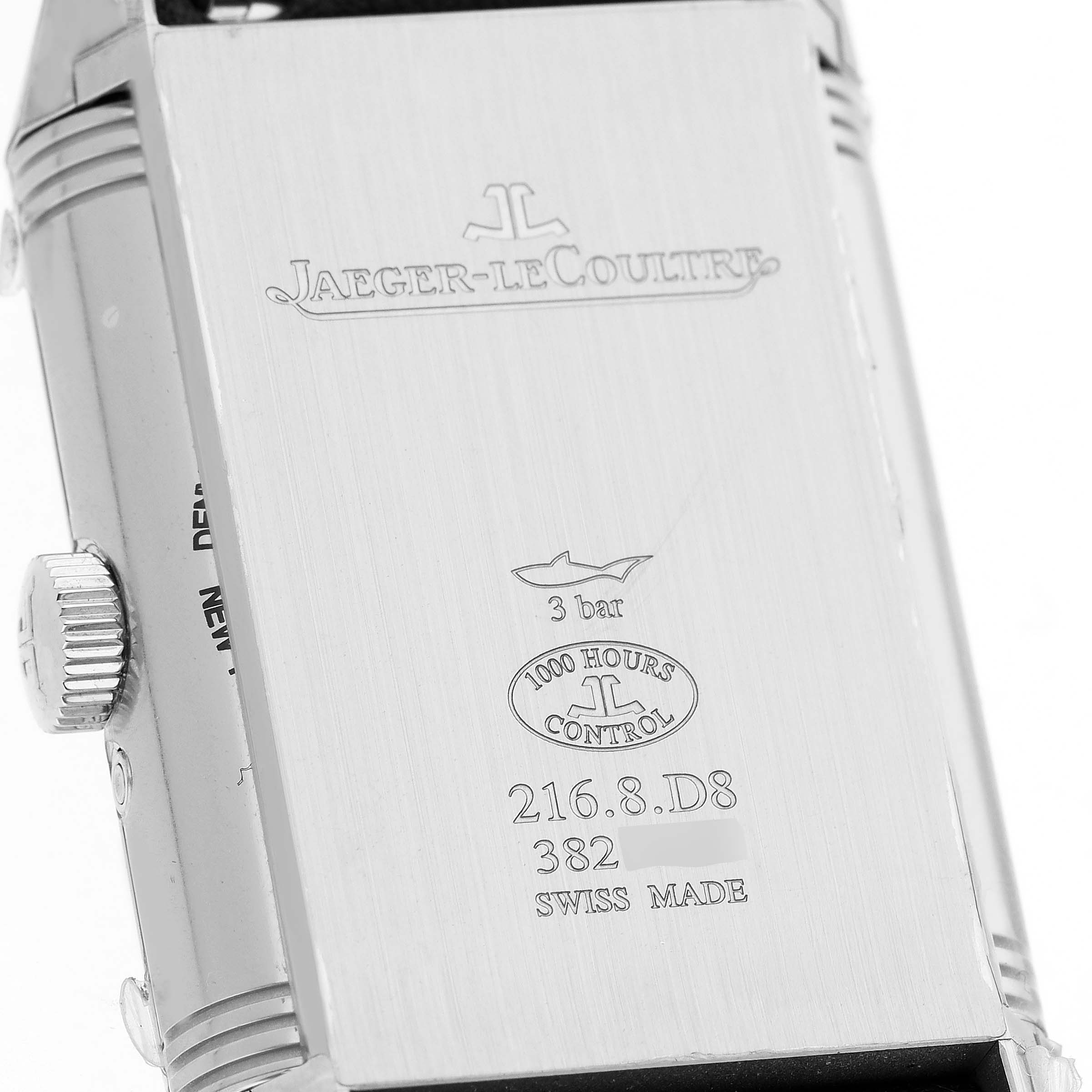 The image shows the backside of a Jaeger-LeCoultre Reverso watch, highlighting engravings and the crown on the side.