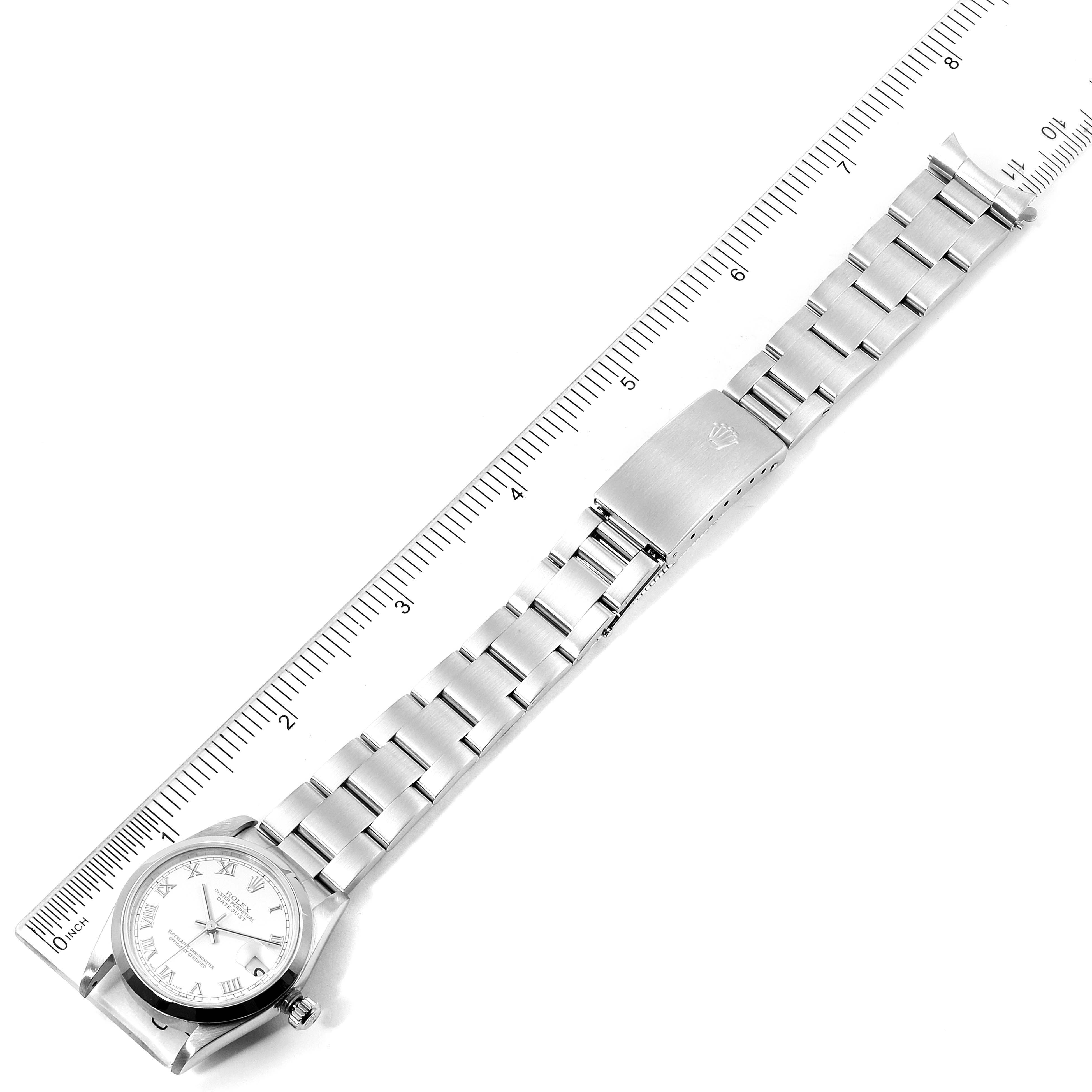 This image shows a top-down view of a Rolex Mid-Size 78240 Women's Stainless Steel White Dial 78240 Women's Stainless Steel White Dial watch with a metal bracelet laid next to a ruler.