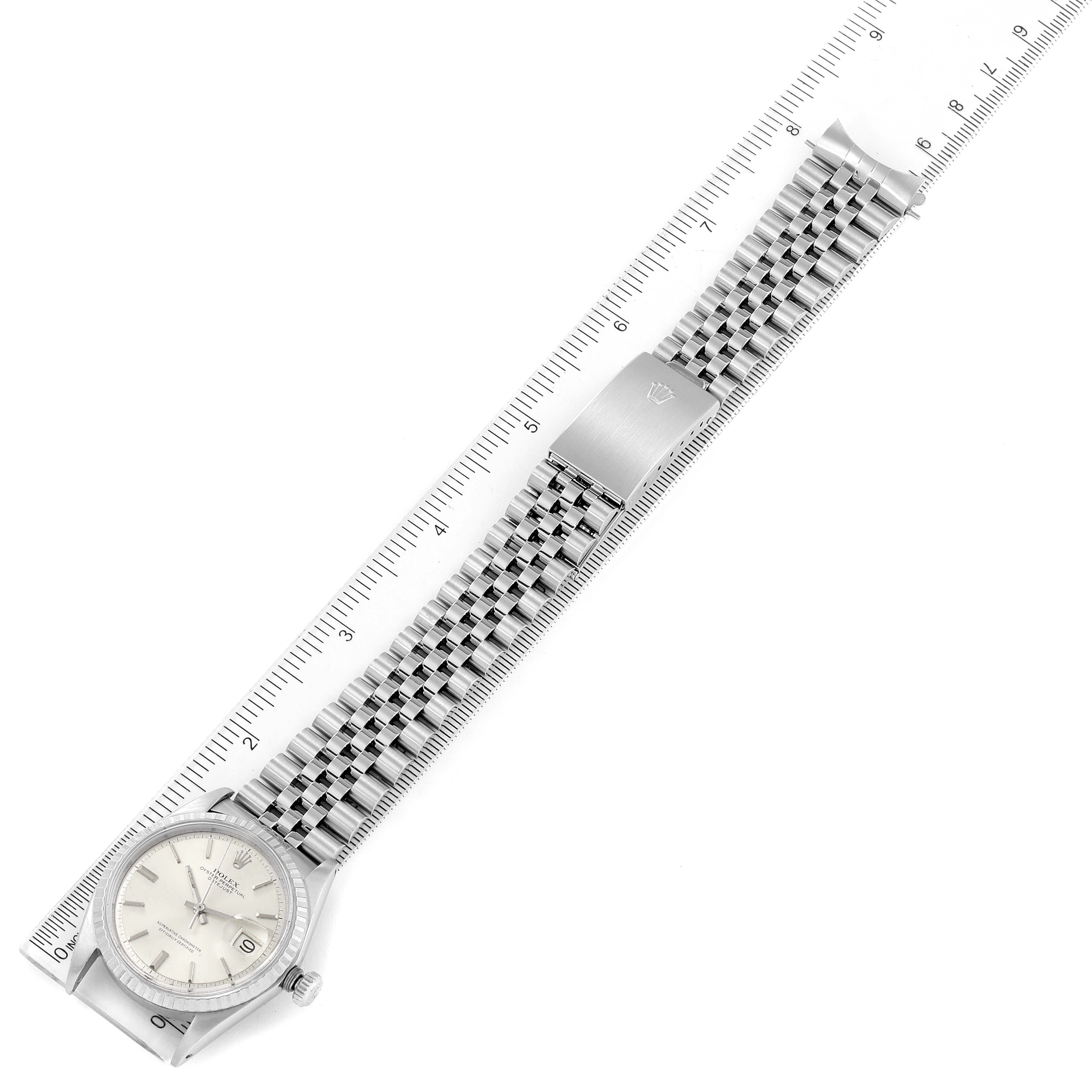 The Rolex Datejust 1603 Men
s Stainless Steel Silver Dial 1603 Men
s Stainless Steel Silver Dial watch is shown from a top view, displaying its face, Jubilee bracelet, and clasp, alongside a ruler for scale.