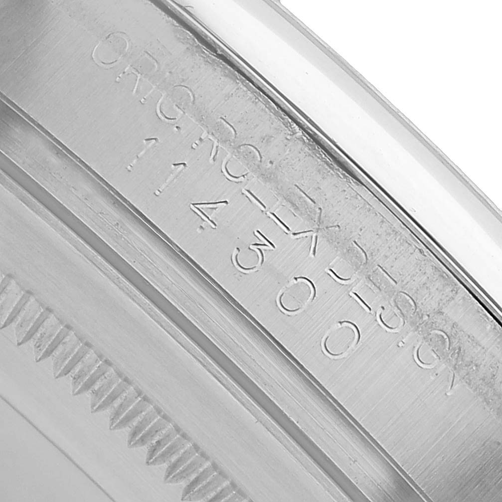 The image shows a close-up of the inner bezel engraving on a Rolex Oyster Perpetual 114300 Men's Stainless Steel Blue Dial watch.