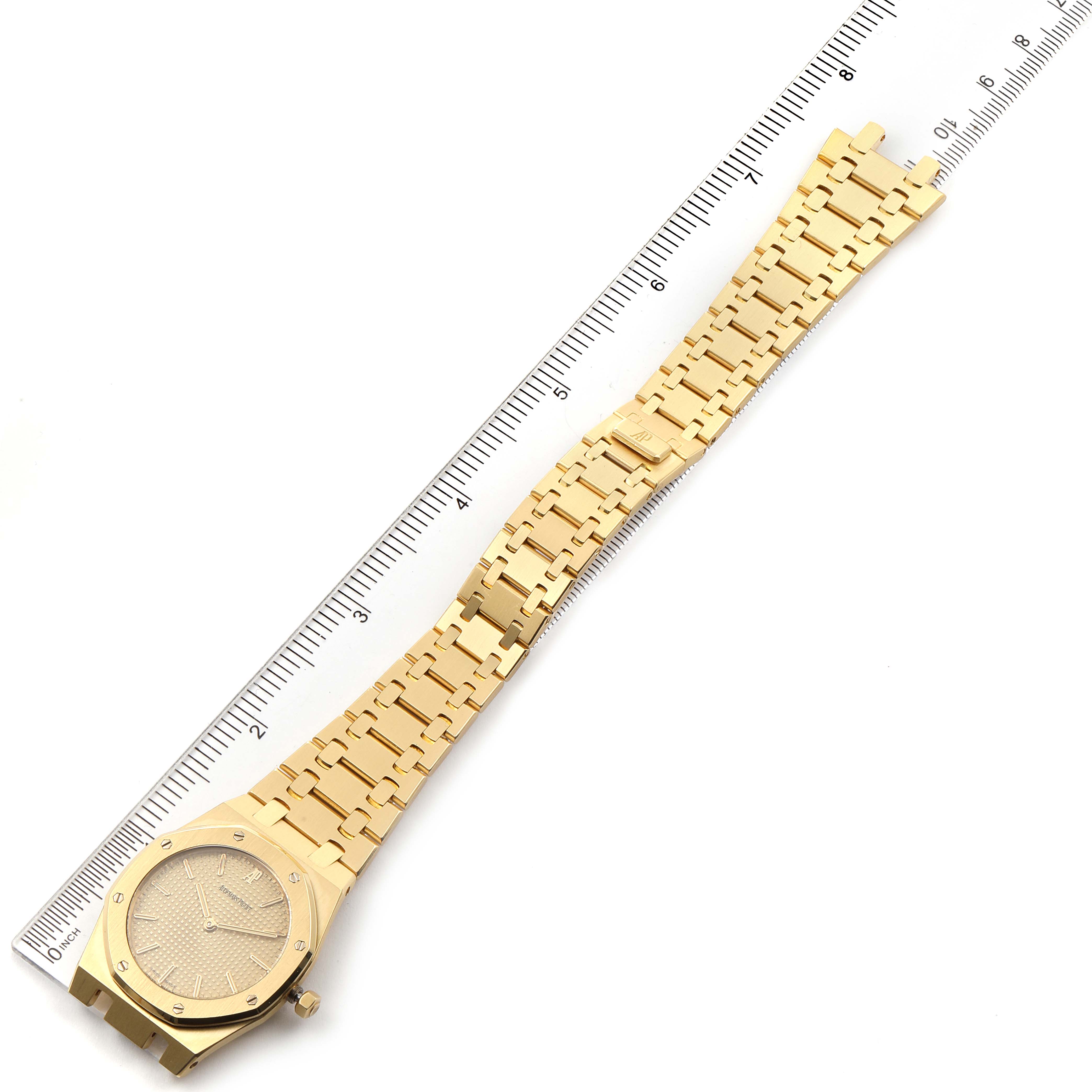 The image shows a top-down view of an Audemars Piguet Royal Oak  Men's Yellow Gold Champagne Dial  Men's Yellow Gold Champagne Dial watch with its bracelet extended alongside a ruler for measurement.