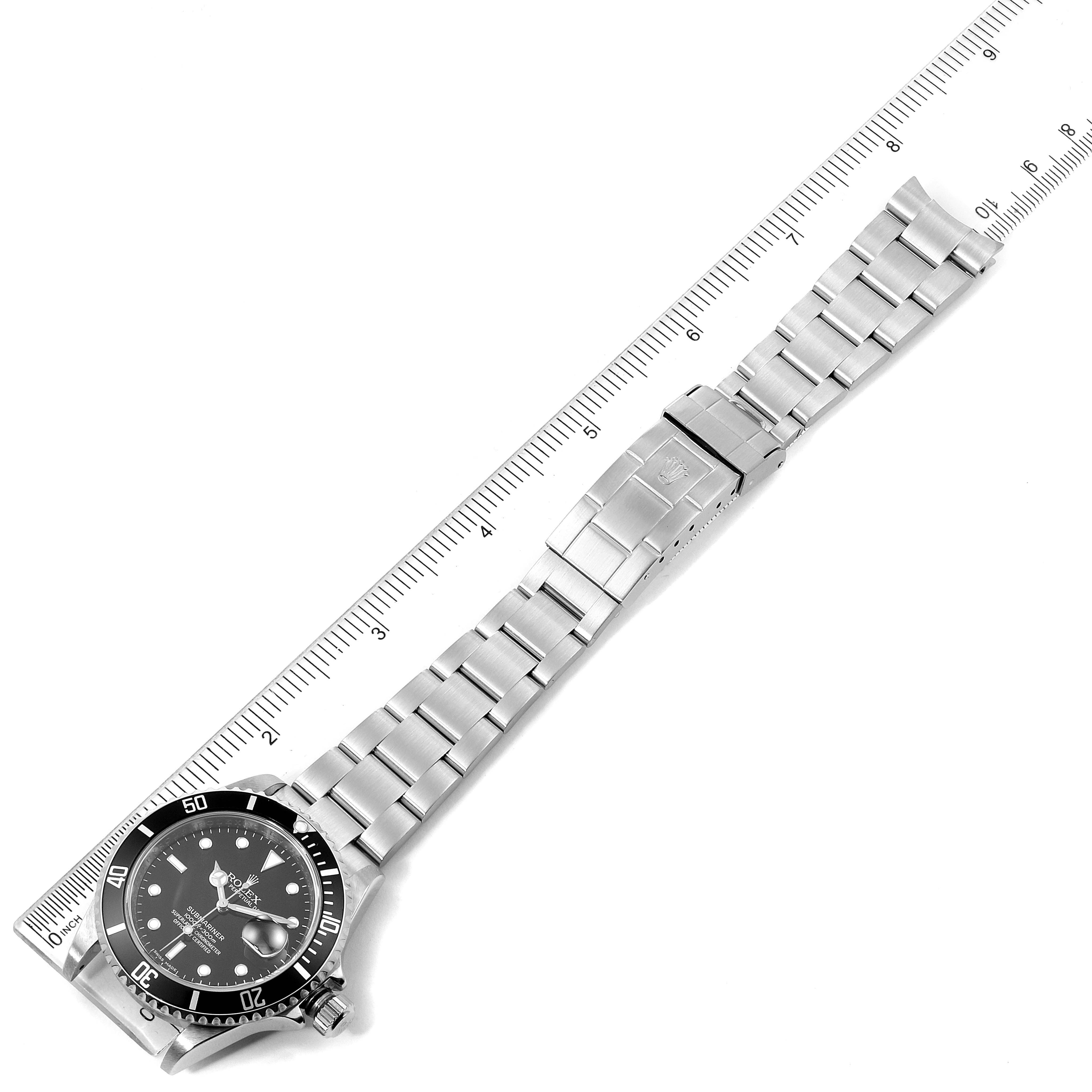 This image shows a Rolex Submariner 16610 Men
s Stainless Steel Black Dial 16610 Men
s Stainless Steel Black Dial watch laid flat alongside a ruler, displaying the watch face, bracelet, and clasp.
