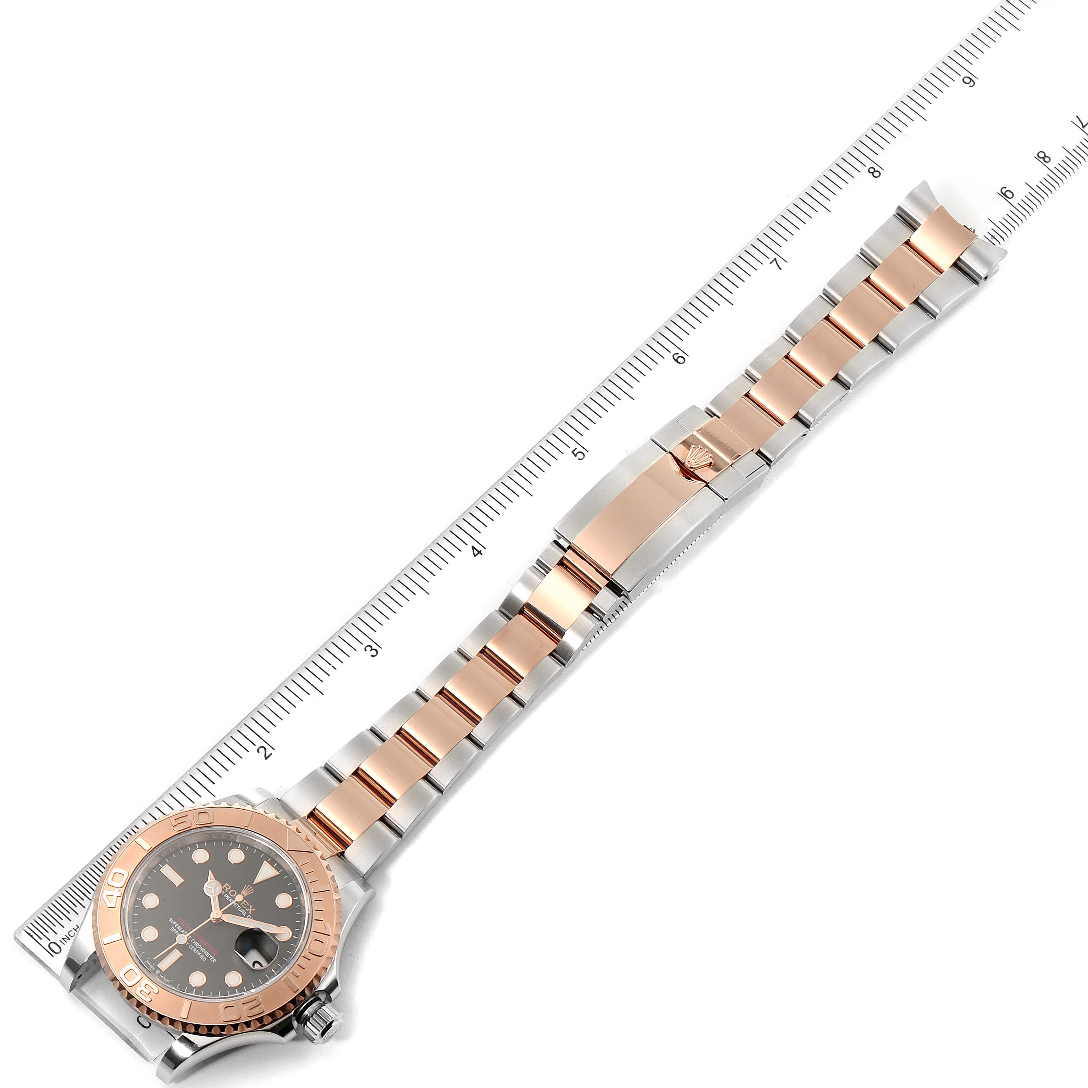 This image shows the front view of the Rolex Yacht-Master 126621 Men
s Steel and Gold (two tone) Black Dial 126621 Men
s Steel and Gold (two tone) Black Dial watch laid next to a ruler, displaying its face and two-tone bracelet.
