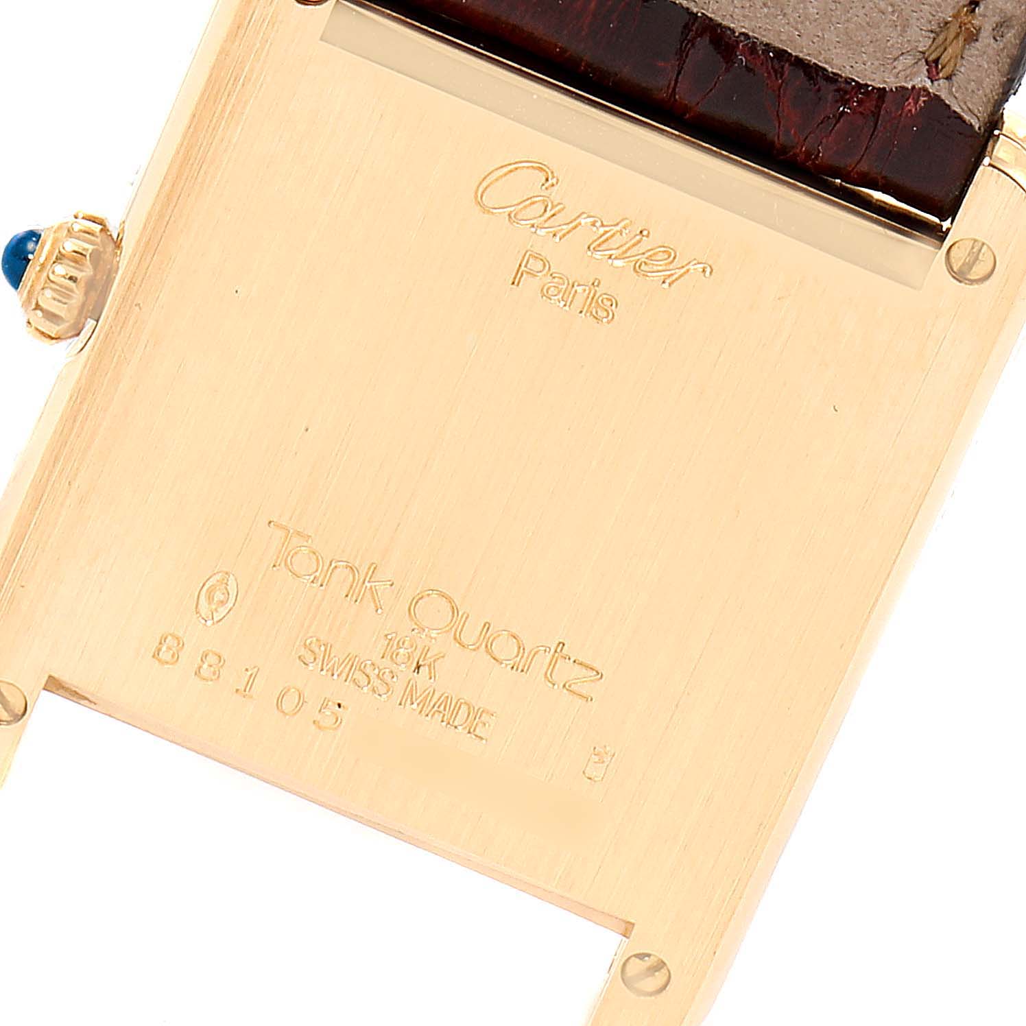The image shows the back case of a Cartier Tank Classic  Women's Yellow Gold White Dial  Women's Yellow Gold White Dial watch featuring inscriptions and a portion of the crown.