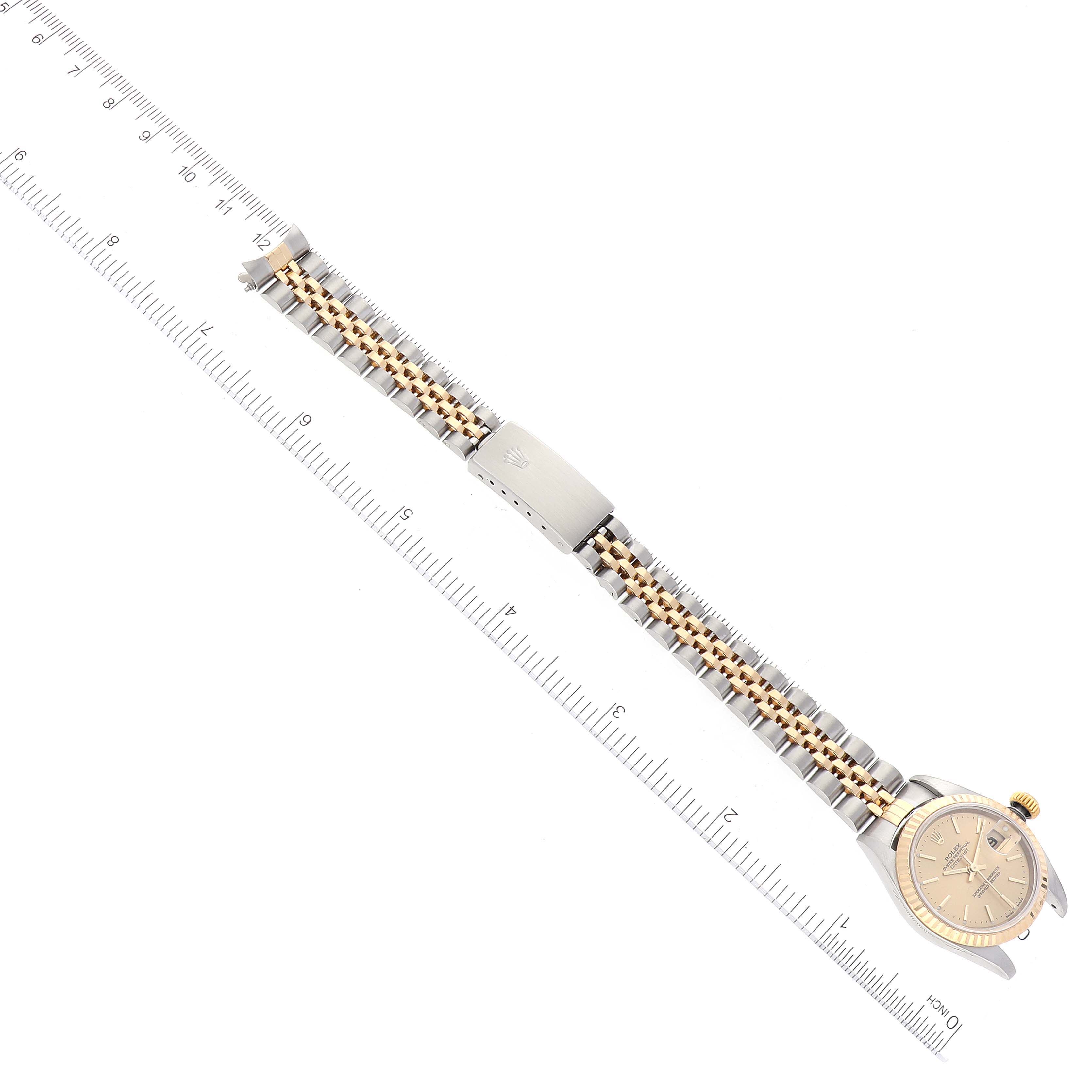 The image shows a top-down view of a Rolex Datejust 79173 Women's Steel and Gold (two tone) Champagne Dial 79173 Women's Steel and Gold (two tone) Champagne Dial watch with its metal bracelet and clasp next to a ruler.