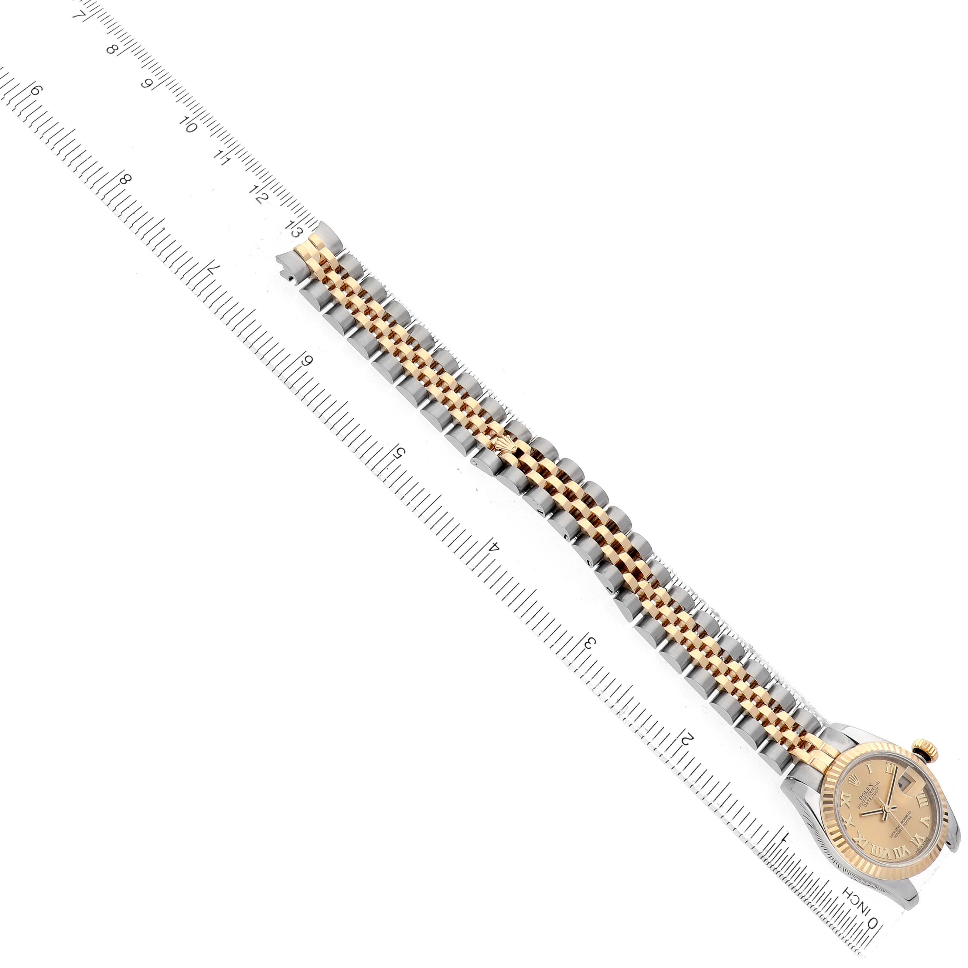 The Rolex Datejust 179173 Women's Steel and Gold (two tone) Champagne Dial is displayed diagonally, showing the bracelet and dial next to a ruler for scale.