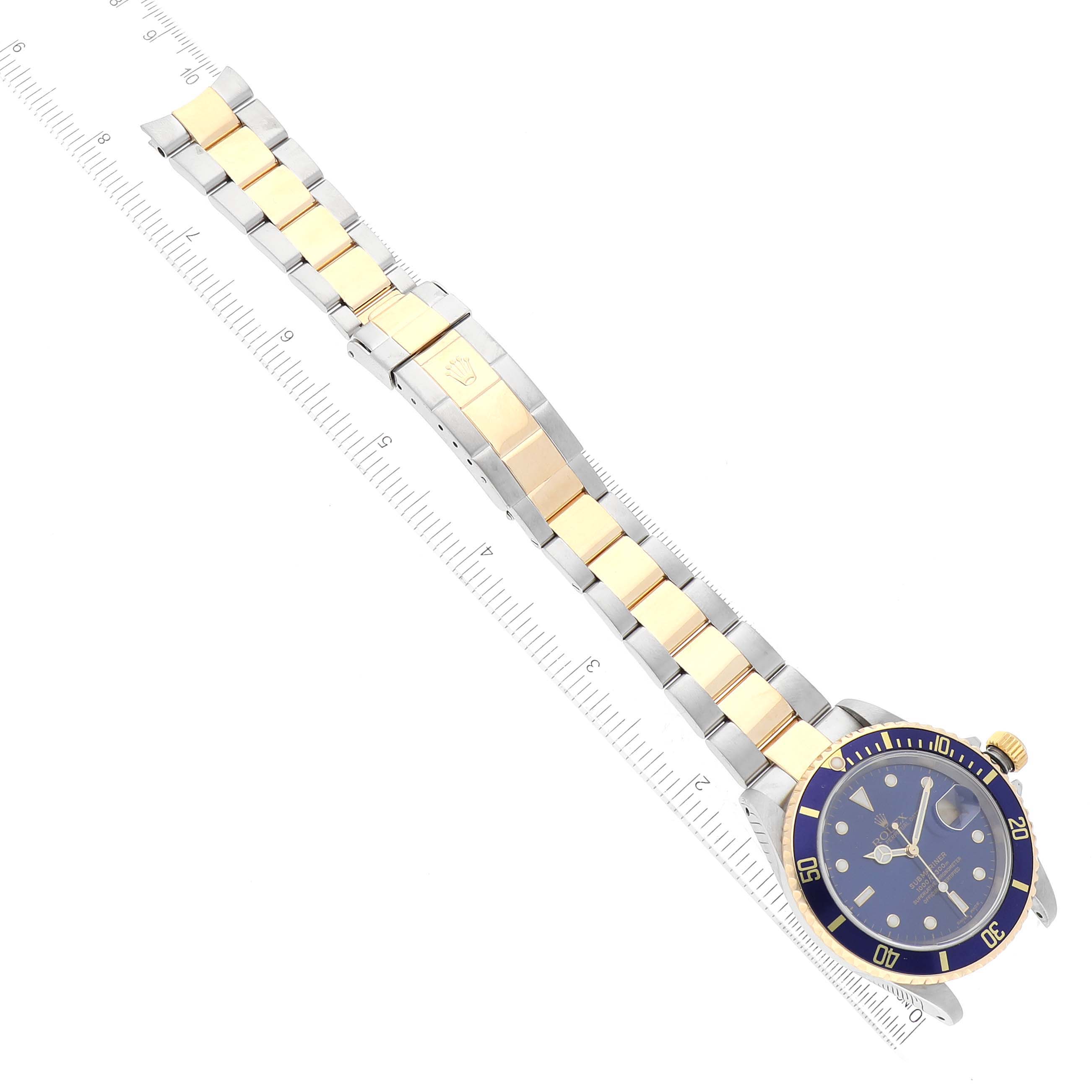 The image shows a top-view angle of a Rolex Submariner 16613 Men
s Steel and Gold (two tone) Blue Dial 16613 Men
s Steel and Gold (two tone) Blue Dial watch, featuring its face, bezel, and two-tone bracelet next to a ruler.