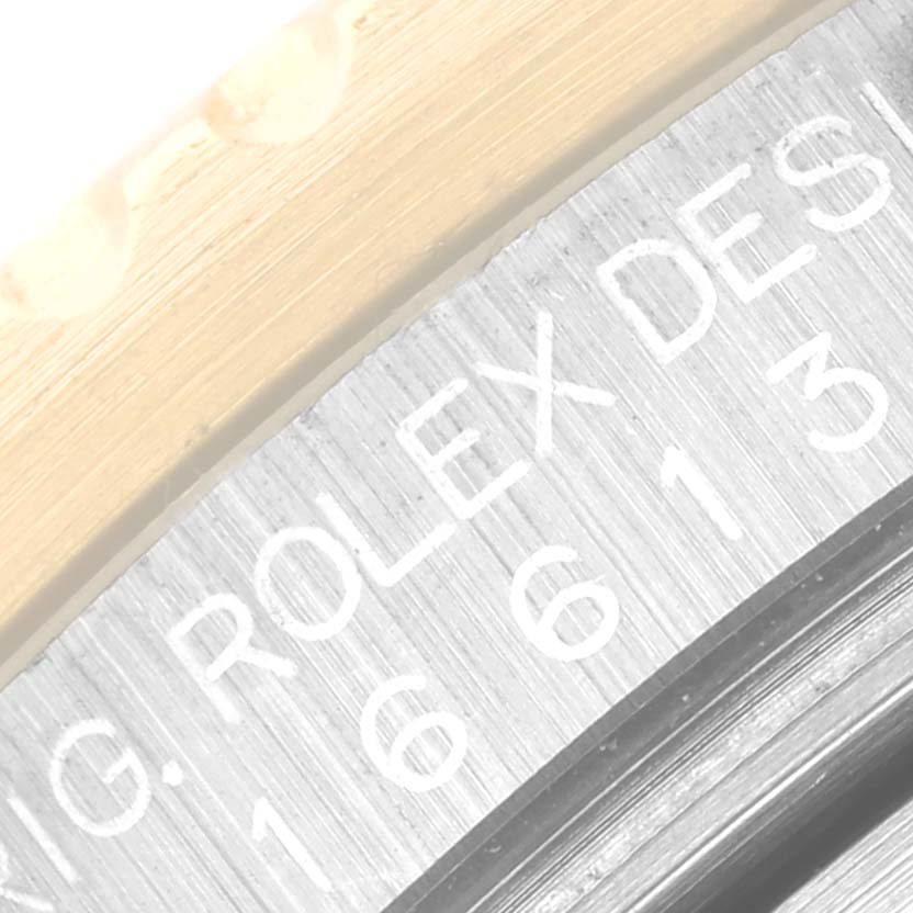 The image shows a close-up of the model and brand engraving on the edge of a Rolex Submariner 16613 Men
s Steel and Gold (two tone) Blue Dial 16613 Men
s Steel and Gold (two tone) Blue Dial watch, focusing on the "Rolex Design" text.