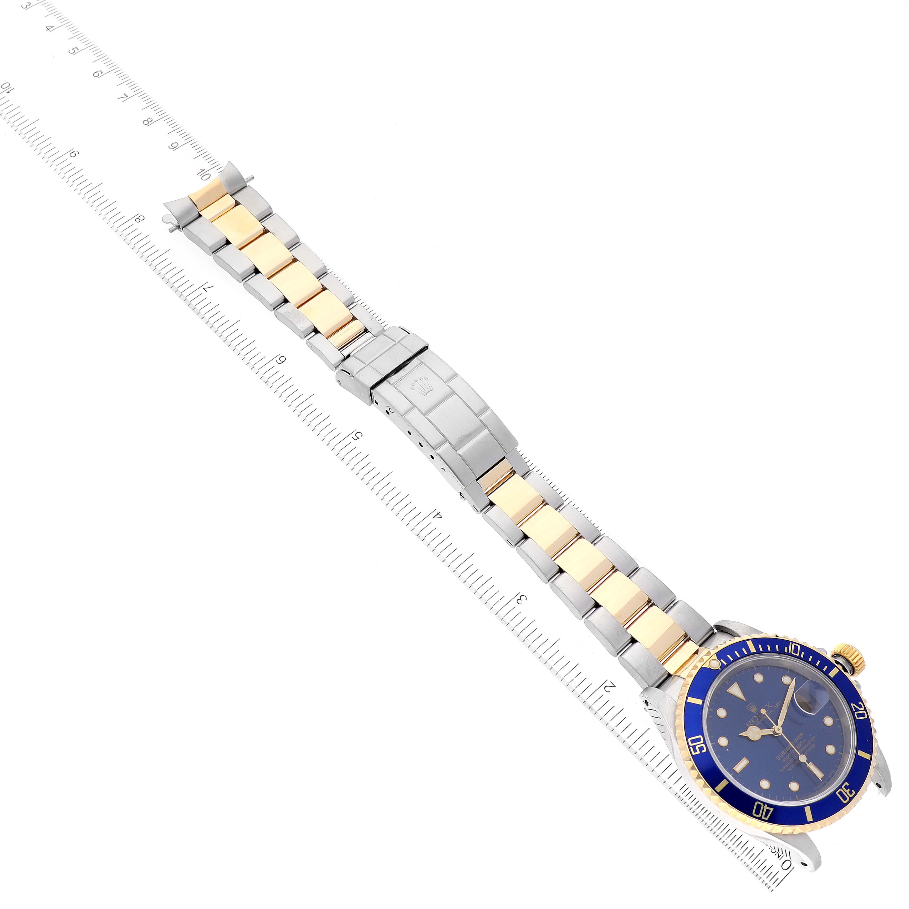 The image shows a Rolex Submariner 16613 Men
s Steel and Gold (two tone) Blue Dial 16613 Men
s Steel and Gold (two tone) Blue Dial watch at an angle with the full view of its bracelet and clasp, aligned with a ruler.