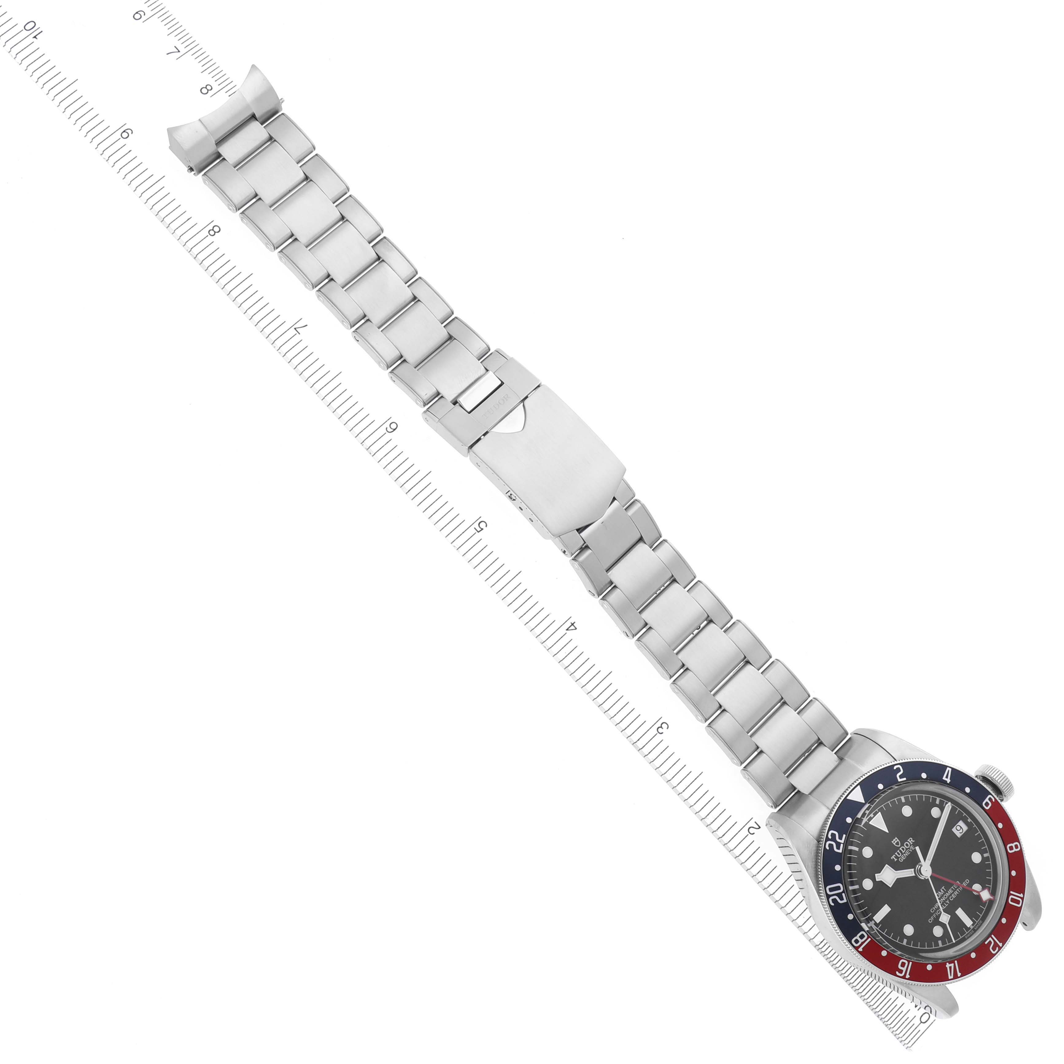 The Tudor Heritage Black Bay 79830RB Men's Stainless Steel Black Dial 79830RB Men's Stainless Steel Black Dial watch is shown at an angle displaying the full bracelet and partly open clasp with a ruler beside it.