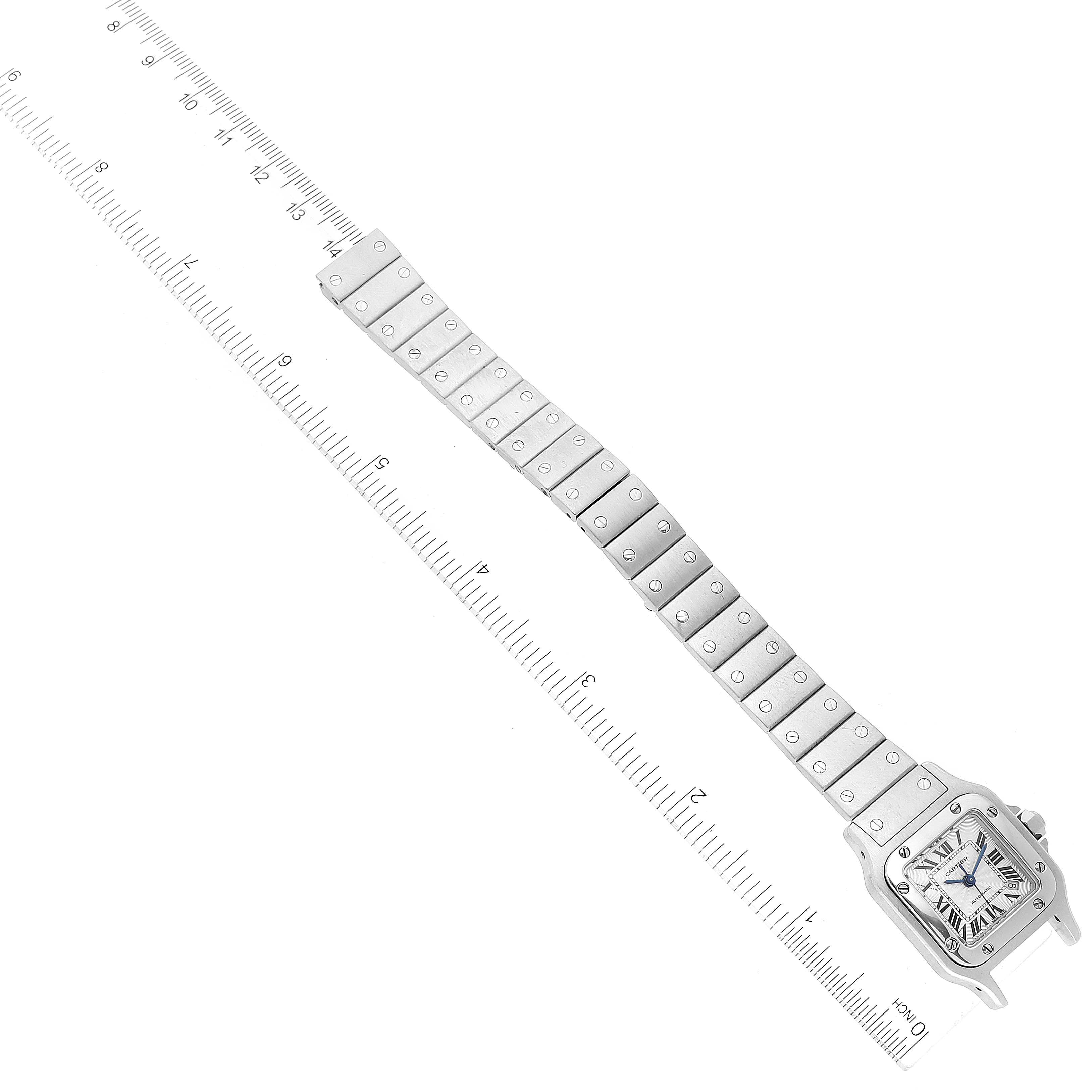 The image shows an overhead view of a Santos model by Cartier, including its face and full metal bracelet next to a ruler.