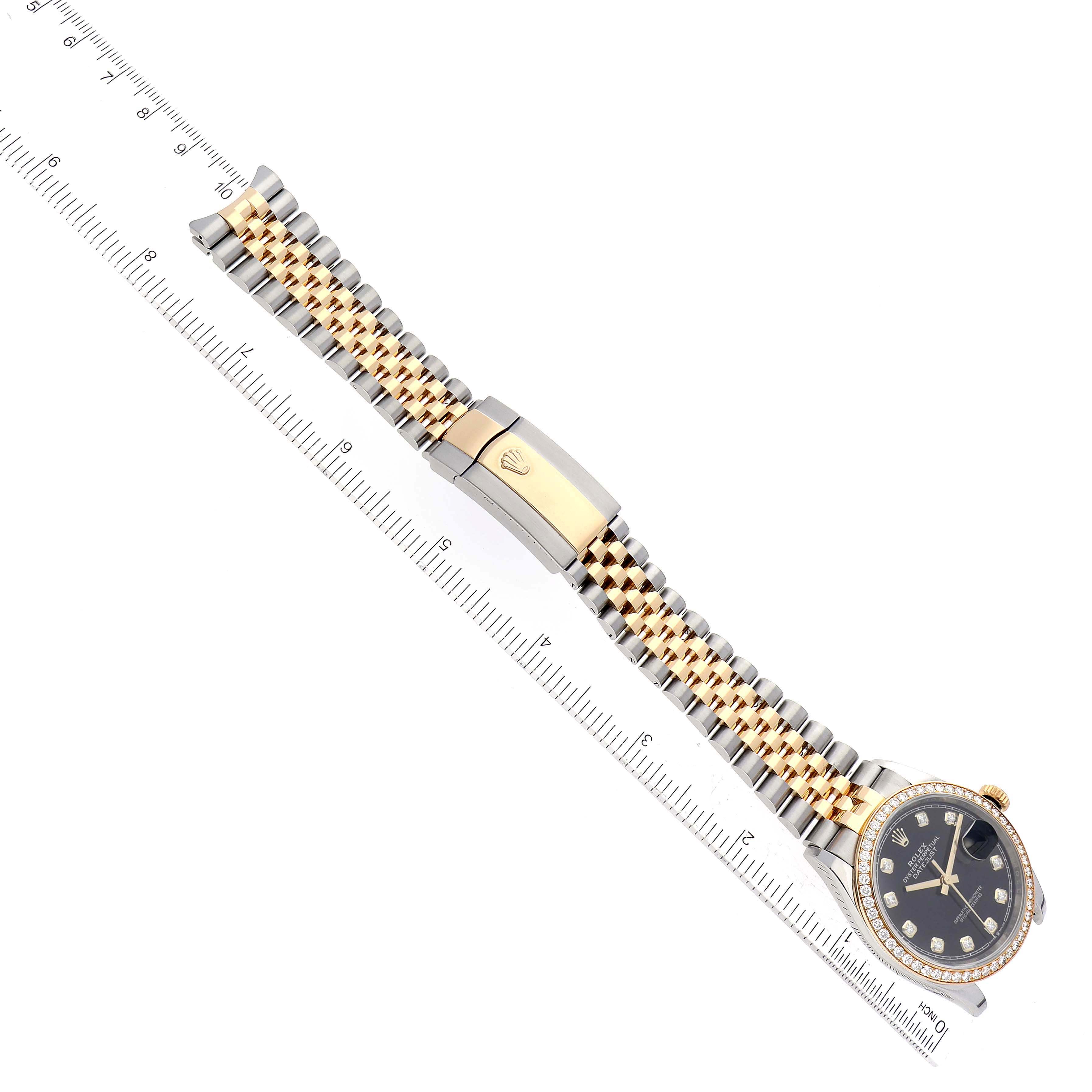 The image shows a Rolex Datejust 126283RBR Men's Steel and Gold (two tone) Black Dial 126283RBR Men's Steel and Gold (two tone) Black Dial watch from a top-down angle, highlighting its bracelet, clasp, and face beside a ruler.