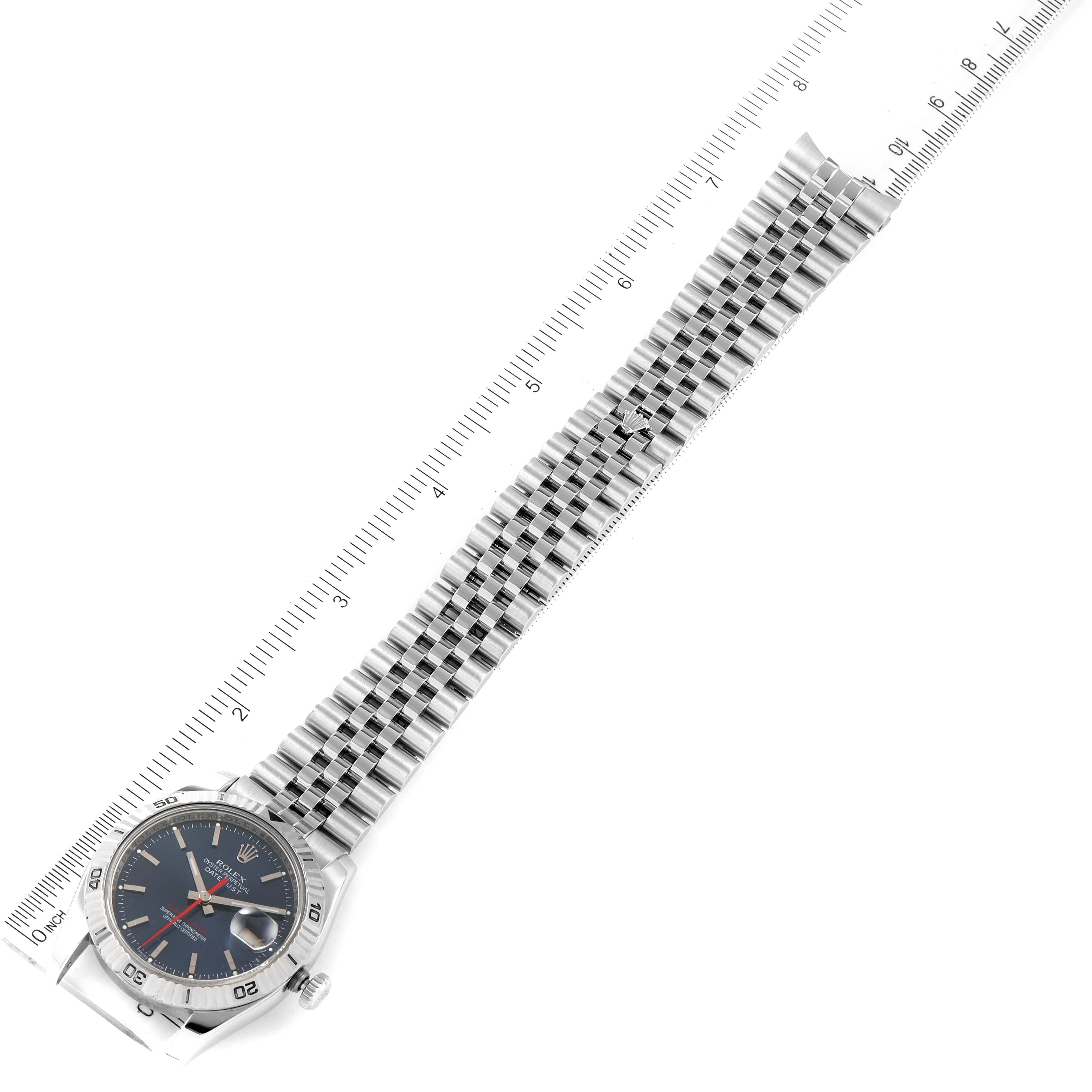 The Rolex Turn-o-Graph 116264 Men
s Stainless Steel Blue Dial 116264 Men
s Stainless Steel Blue Dial watch is shown at an angle displaying the face, bezel, crown, and full length of the metal bracelet next to a ruler.