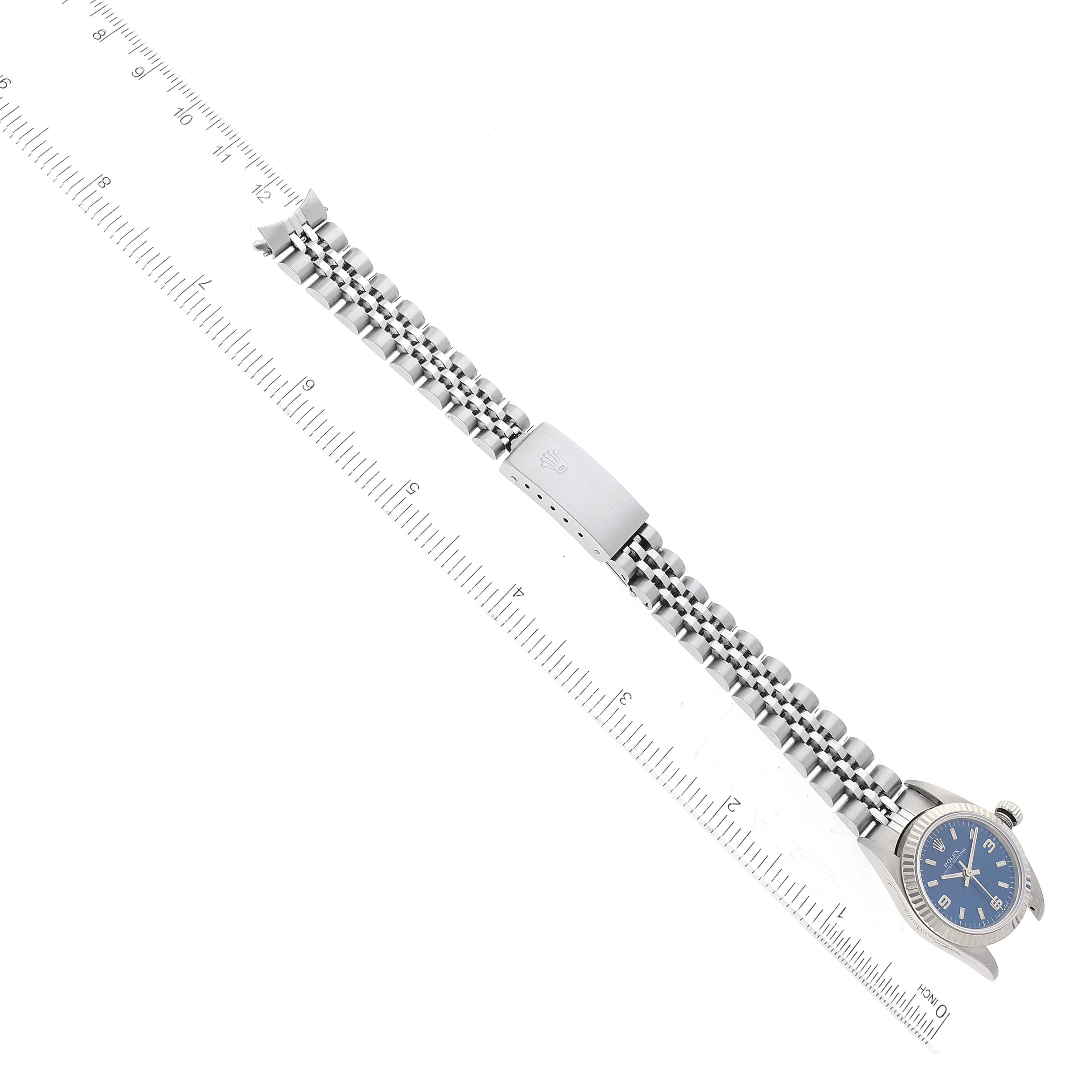 The image shows a Rolex Oyster Perpetual 76094 Women's Stainless Steel Blue Dial 76094 Women's Stainless Steel Blue Dial watch with a blue dial and an expanded view of its metal bracelet, alongside a ruler for scale.