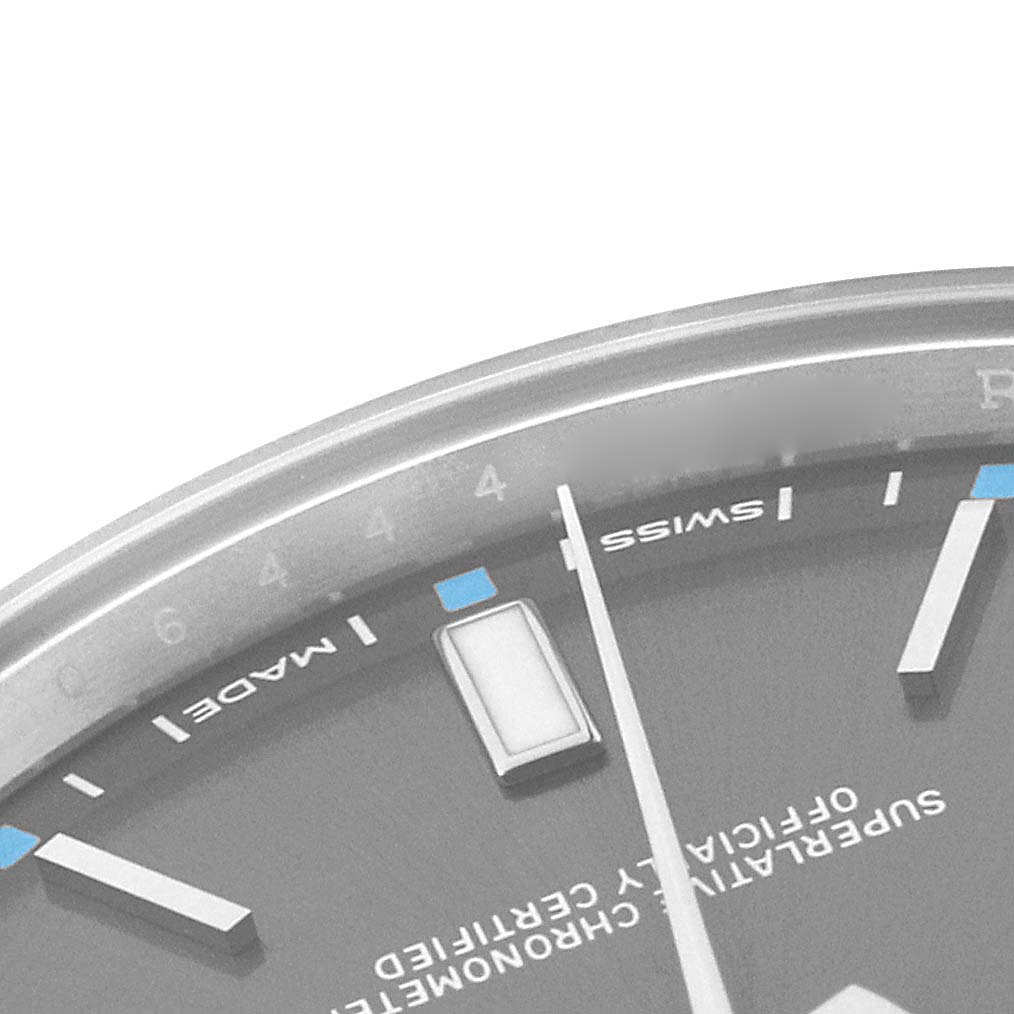 The image shows a close-up of the dial and markers of a Rolex Oyster Perpetual 114300 Men's Stainless Steel Grey Dial 114300 Men's Stainless Steel Grey Dial, focusing on various indices and text.