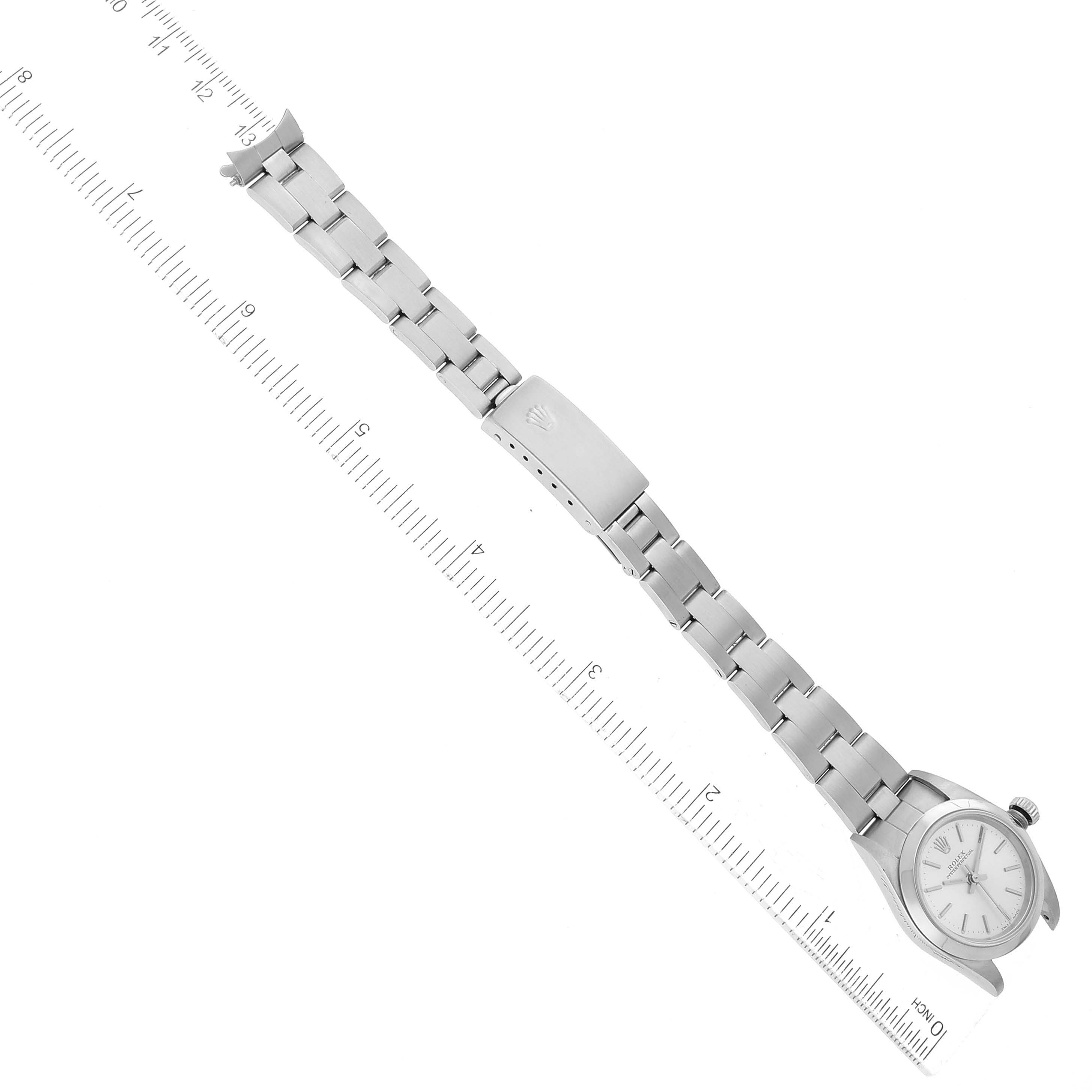 The image shows a top-down view of a Rolex Oyster Perpetual 76080 Women's Stainless Steel Silver Dial 76080 Women's Stainless Steel Silver Dial watch displaying its face, bracelet, and clasp alongside a measuring ruler.