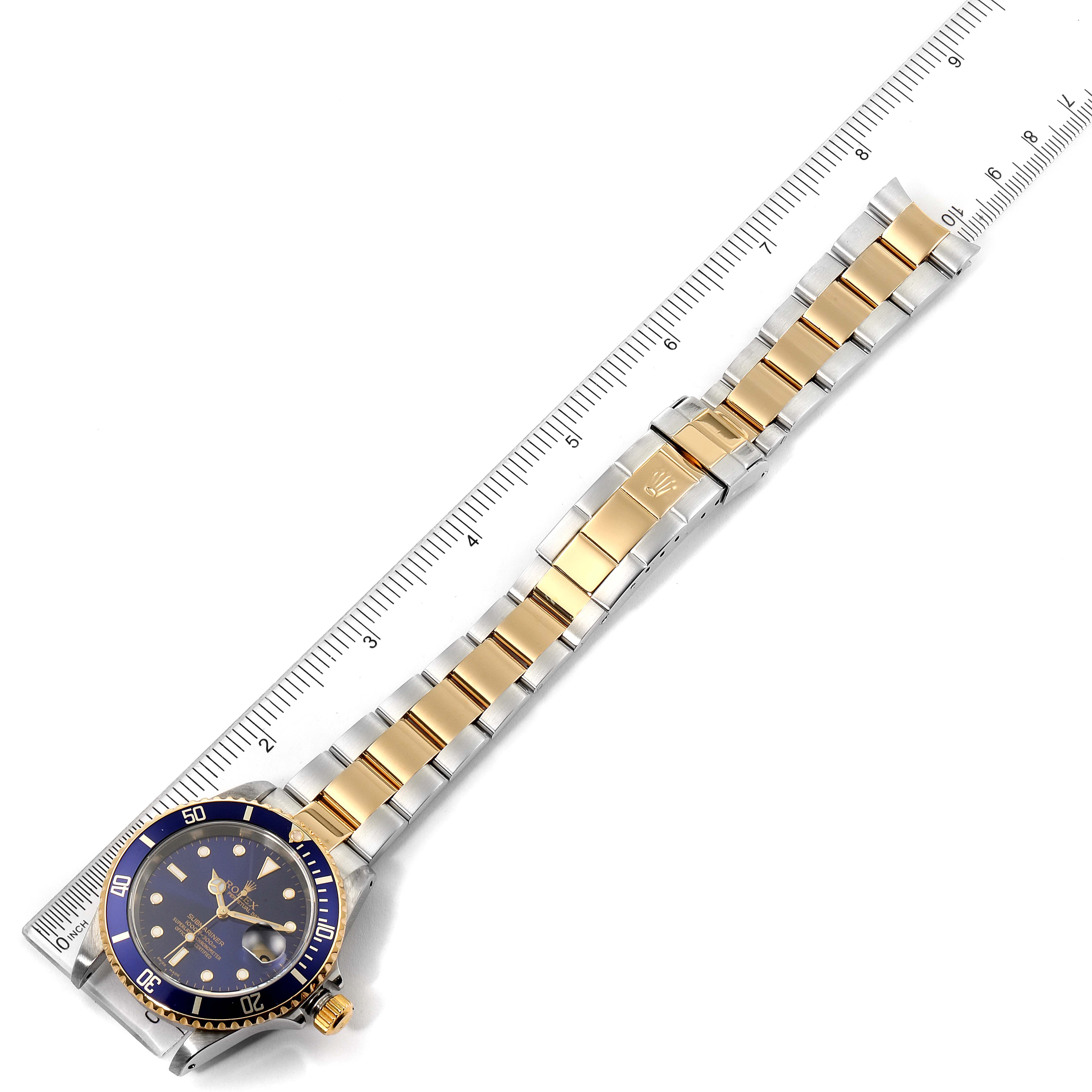 The image shows a top-down view of a Rolex Submariner 16613 Men's Steel and Gold (two tone) Blue Dial 16613 Men's Steel and Gold (two tone) Blue Dial watch, displaying its face, bezel, and full bracelet with a ruler beside it.