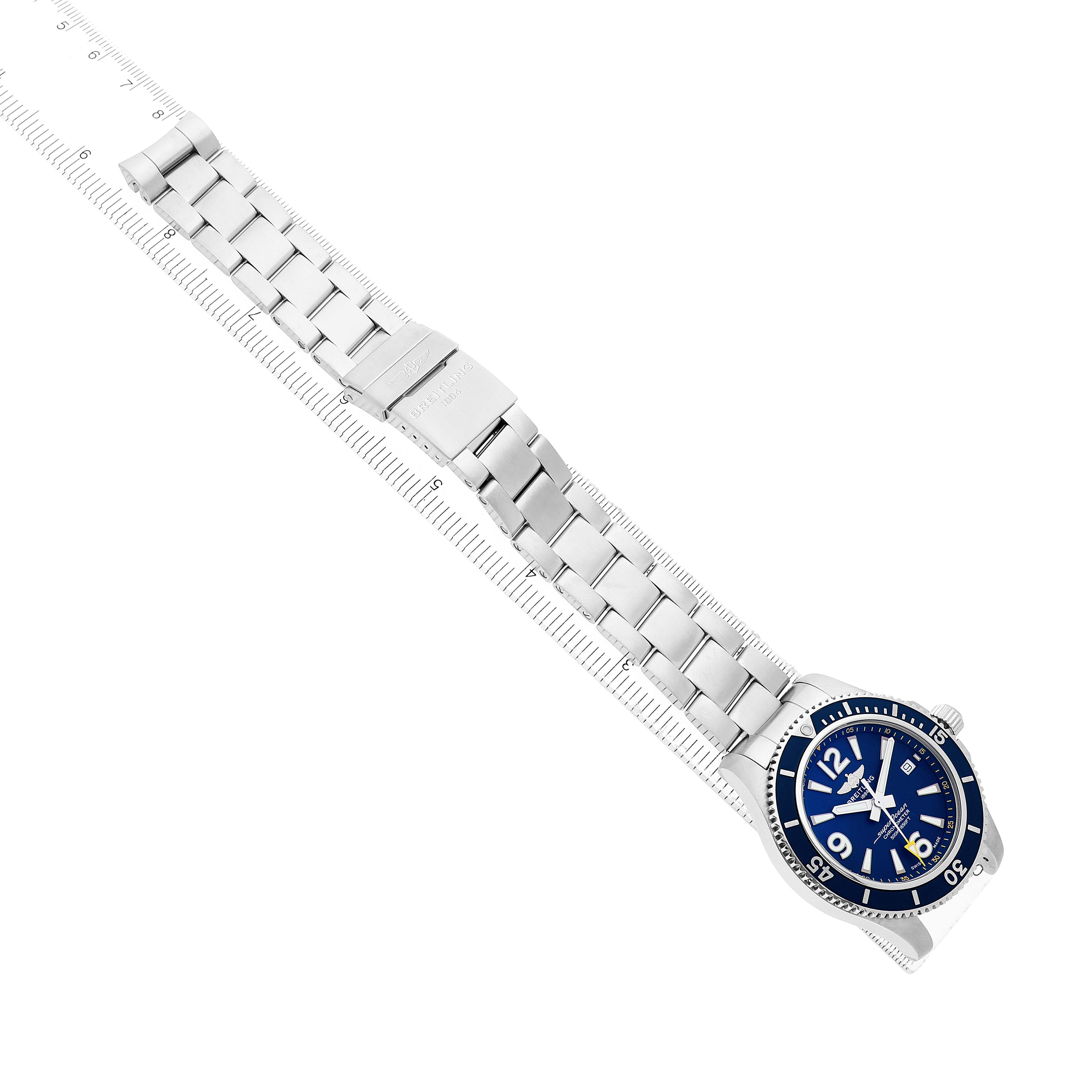 The Breitling Superocean A17366 Men's Stainless Steel Blue Dial watch is shown from an overhead angle, displaying its blue dial, bezel, and metal bracelet on a ruler.