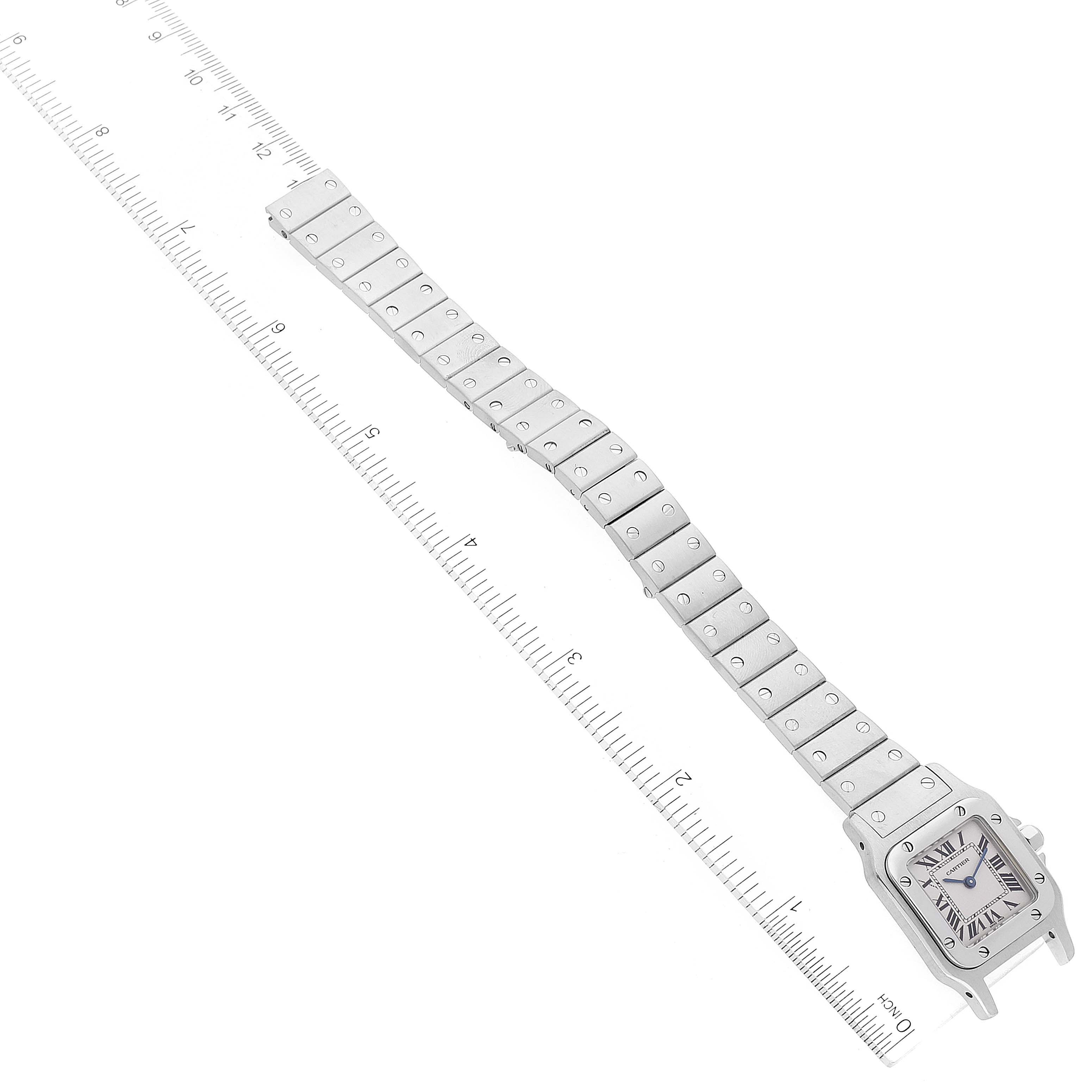 The image shows the face and bracelet of a Santos model by Cartier, positioned diagonally beside a ruler.