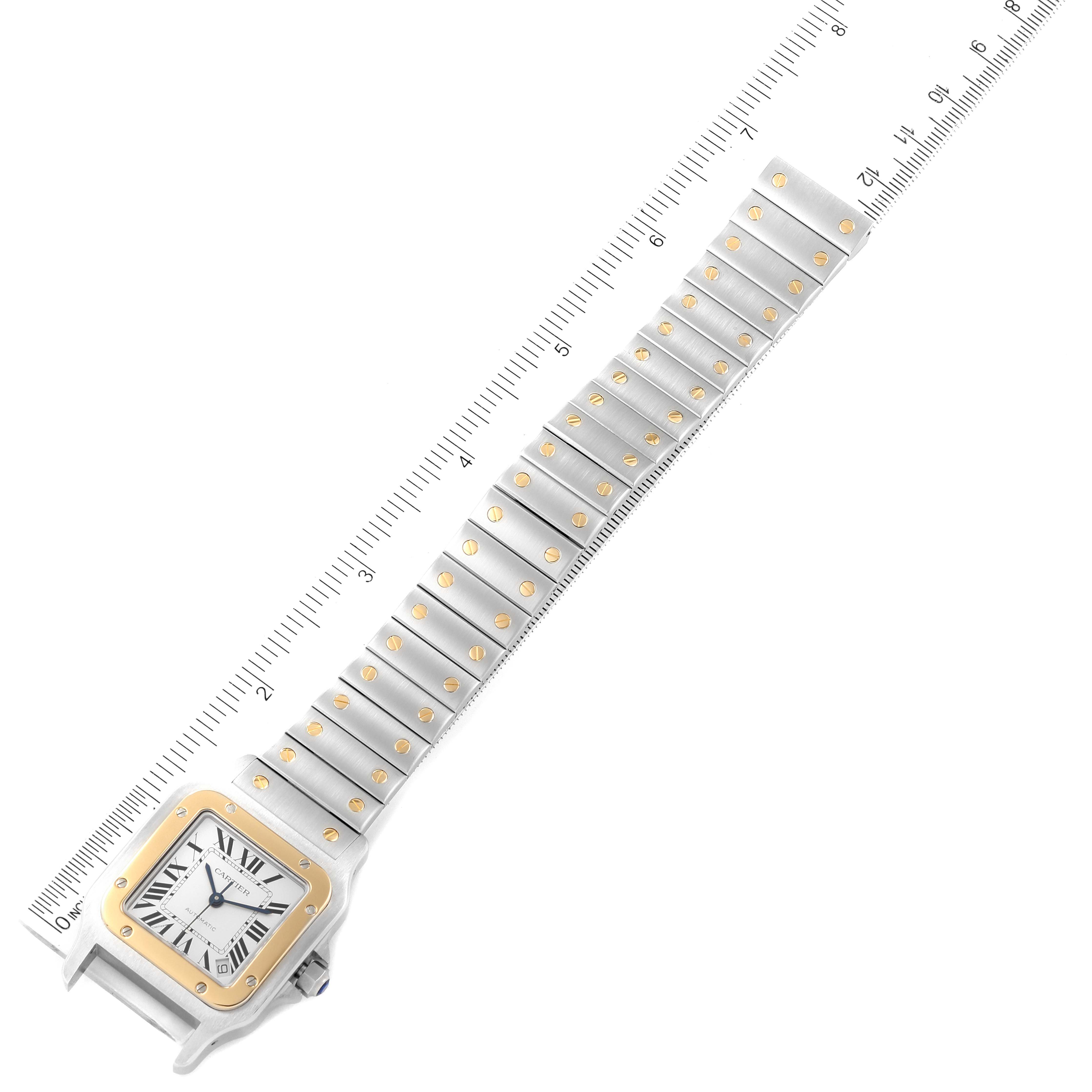 The image shows an overhead view of a Santos model by Cartier, displaying the watch face and entire metal bracelet aligned on a ruler.