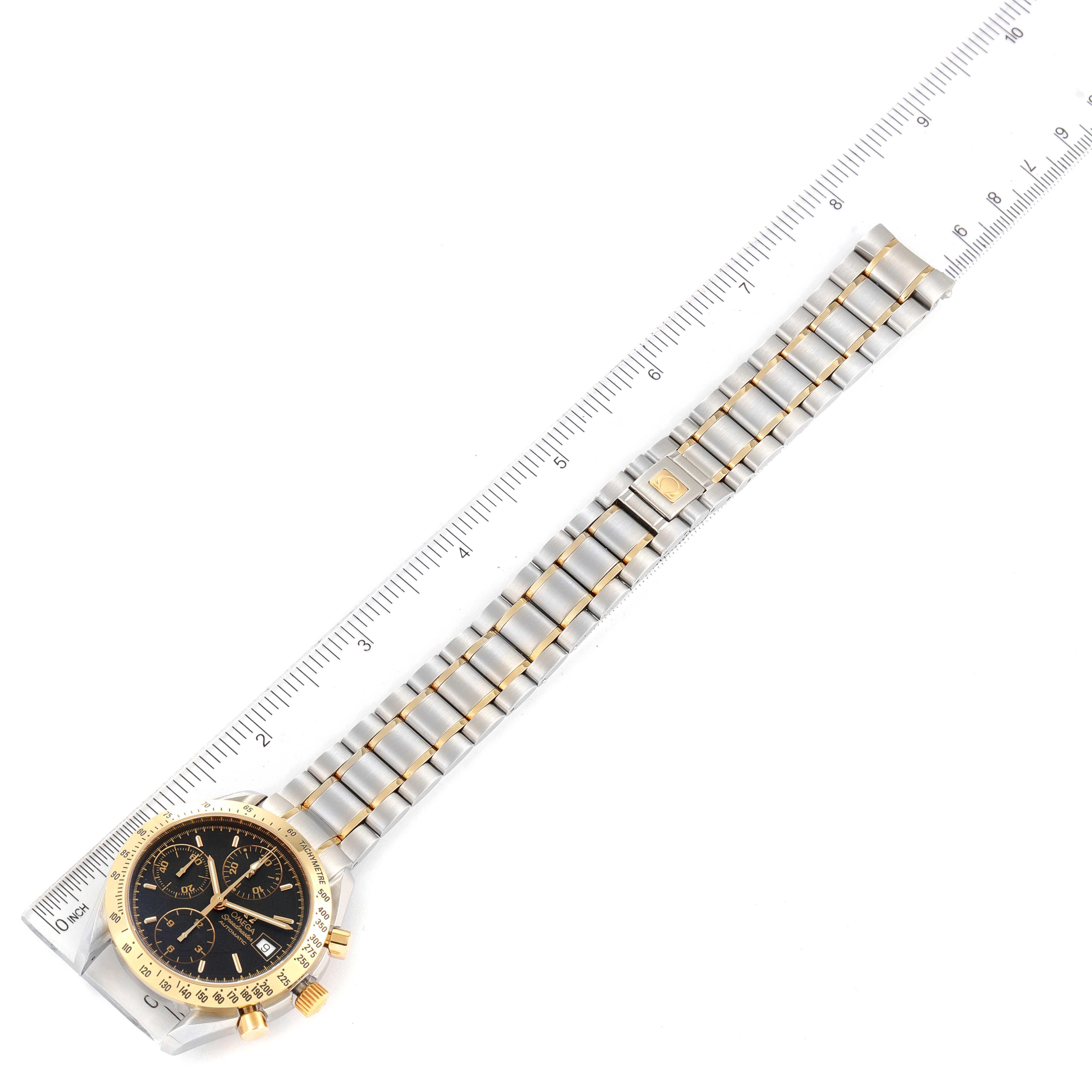 The image shows the front view of an Omega Speedmaster 3313.50.00 Men
s Steel and Gold (two tone) Black Dial 3313.50.00 Men
s Steel and Gold (two tone) Black Dial watch with its bracelet next to a ruler for scale.