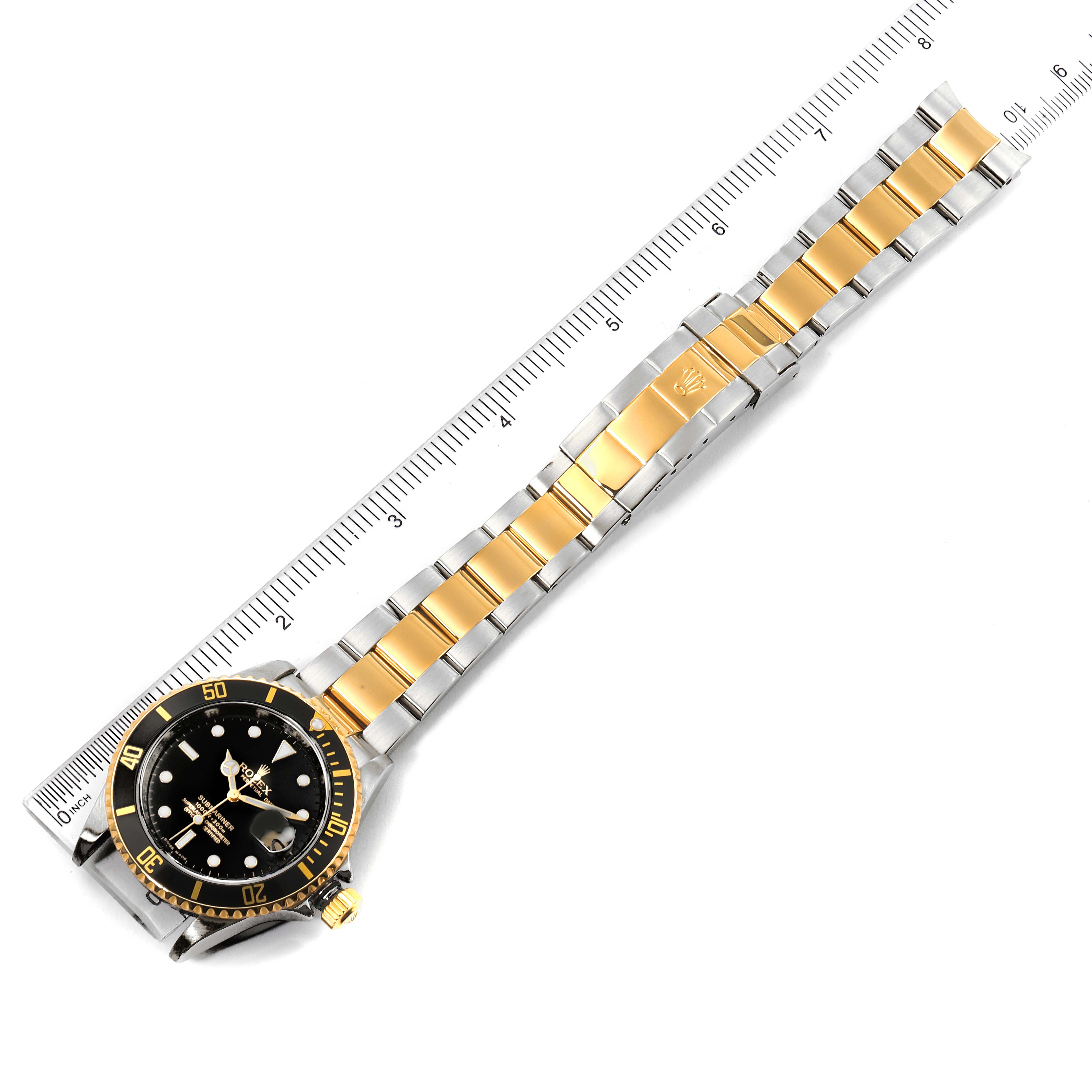 The image shows a Rolex Submariner 16613 Men's Steel and Gold (two tone) Black Dial 16613 Men's Steel and Gold (two tone) Black Dial watch laid flat with its dial, bezel, and two-tone metal bracelet visible, alongside a ruler.