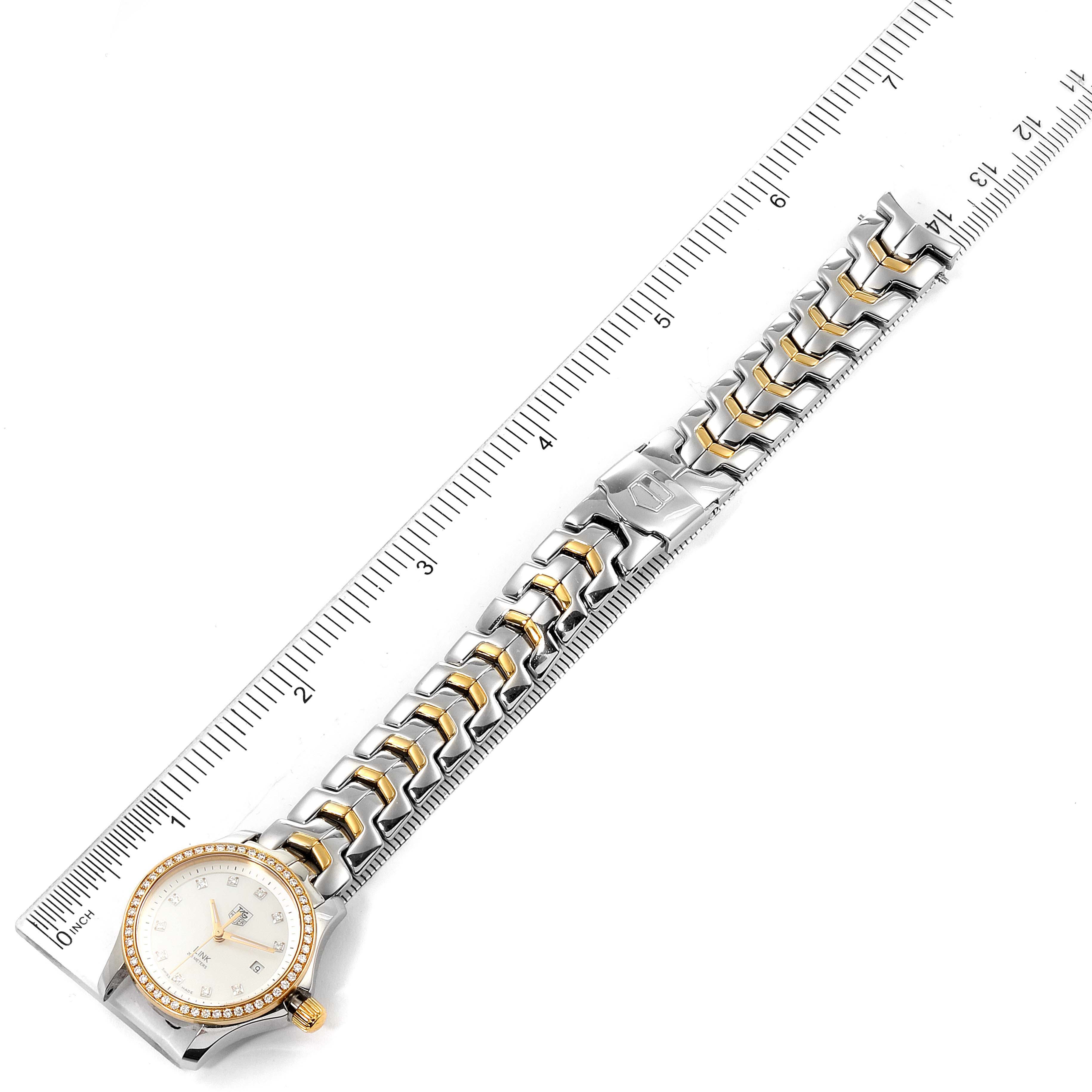 The image shows a top view of a Tag Heuer Link WJF1354.BB0581 Women
s Steel and Gold (two tone) Mother of Pearl Dial WJF1354.BB0581 Women
s Steel and Gold (two tone) Mother of Pearl Dial model watch, including its face and full bracelet, placed next to a ruler.