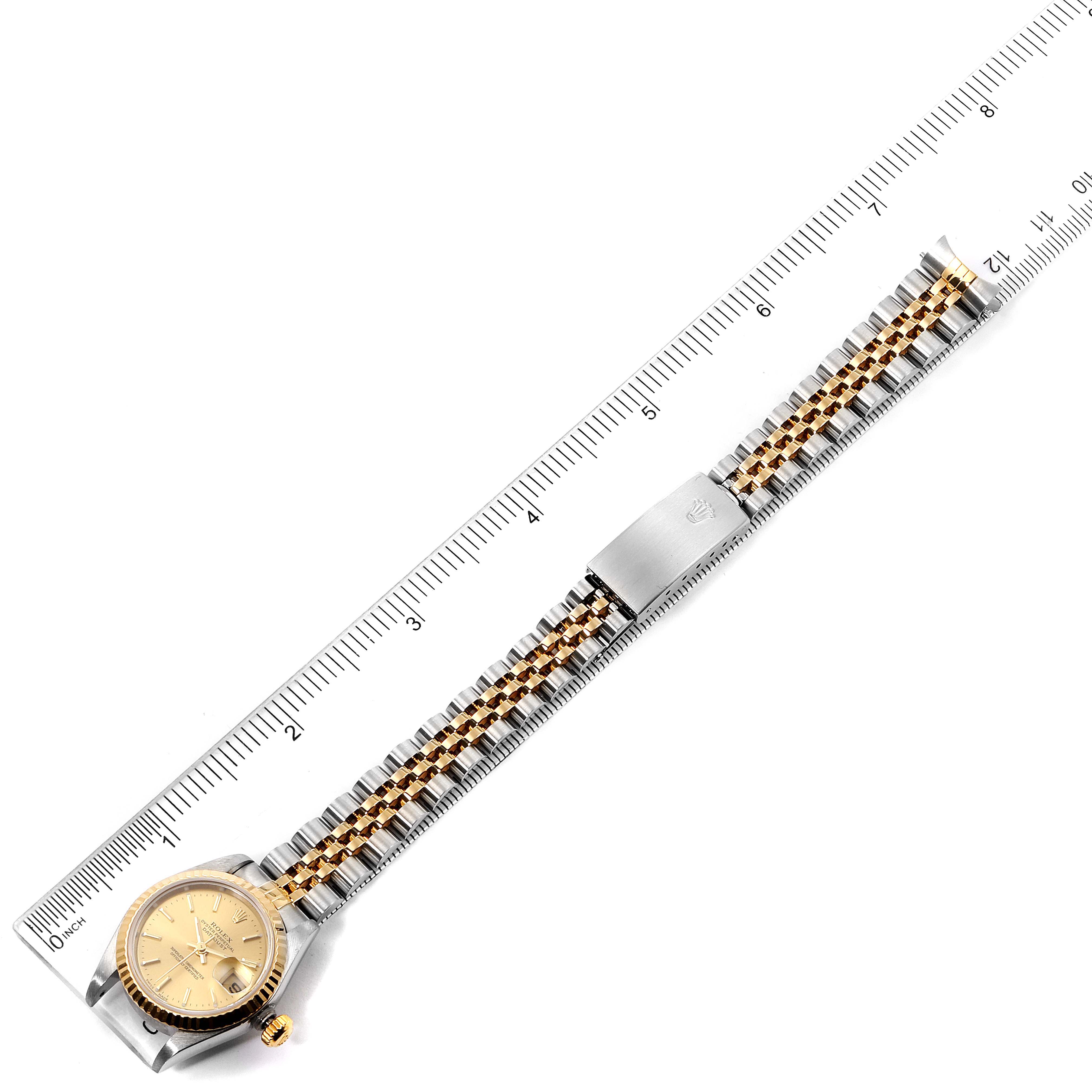 The image shows a top view of a Rolex Datejust 79173 Women's Steel and Gold (two tone) Champagne Dial 79173 Women's Steel and Gold (two tone) Champagne Dial watch displaying its gold dial and two-tone metal bracelet against a ruler.